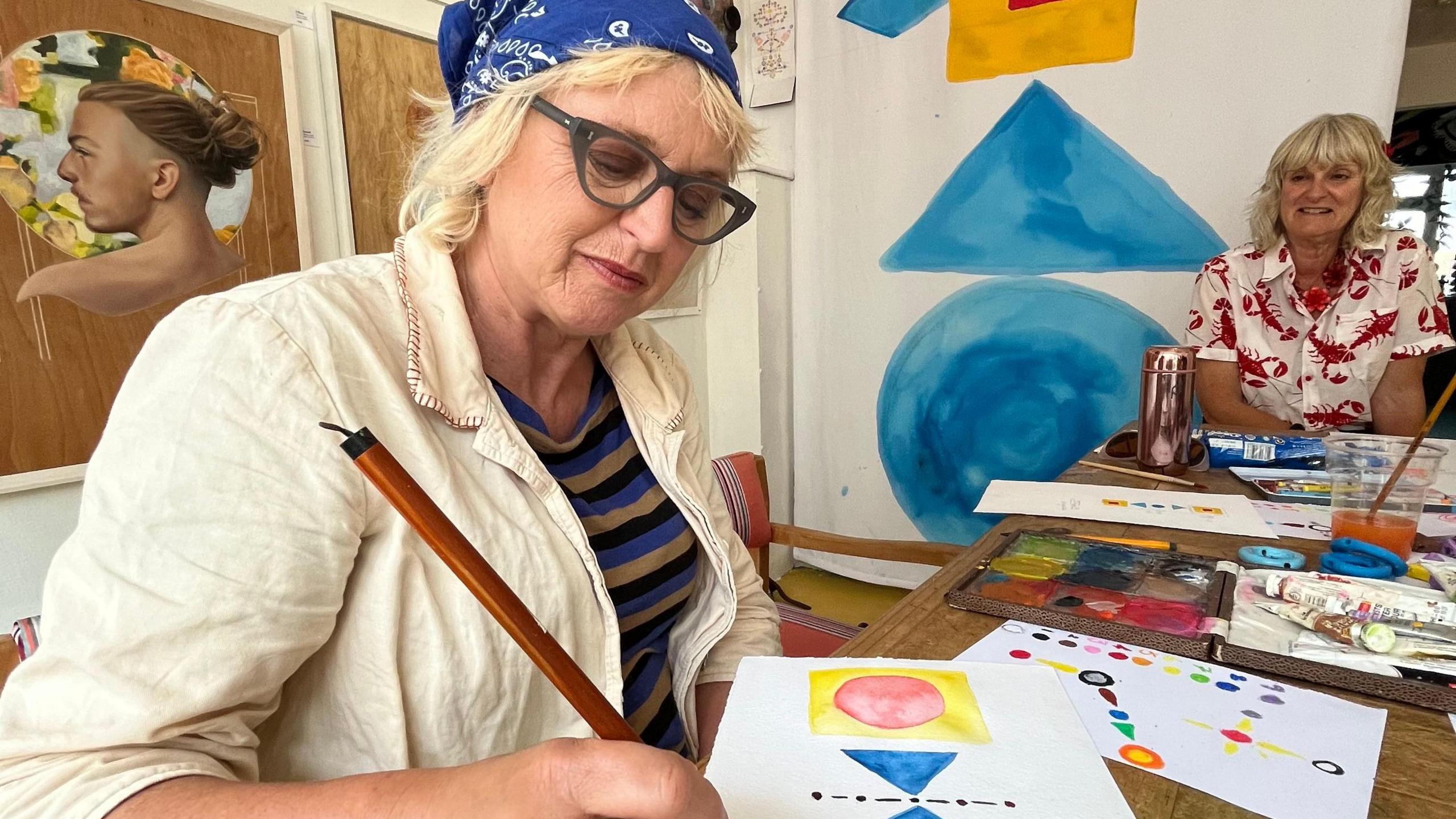 Two older women sat at a table painting using the visual maths method and smiling 