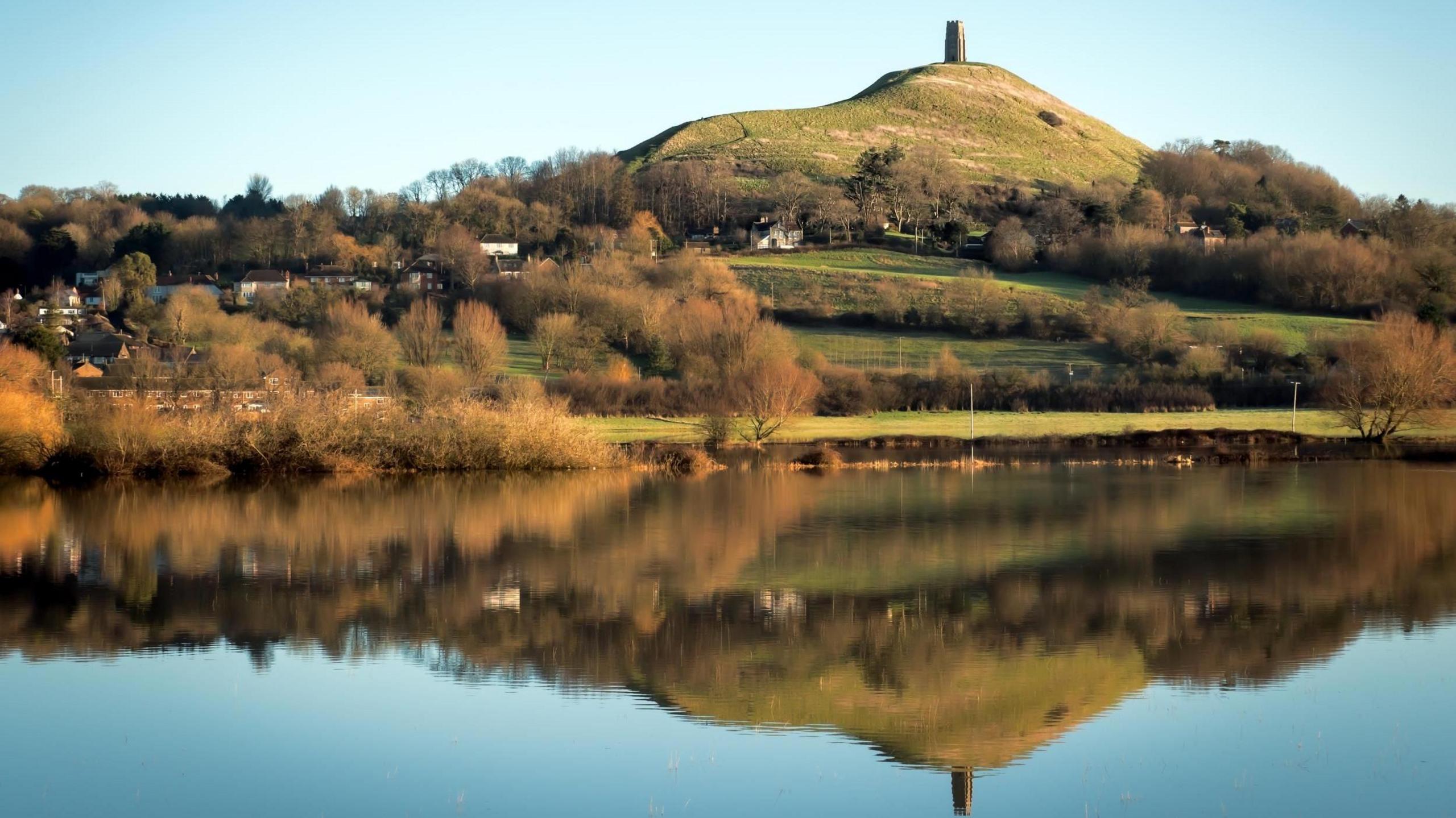 Glastonbury Tor is reflected in the water below the hill.