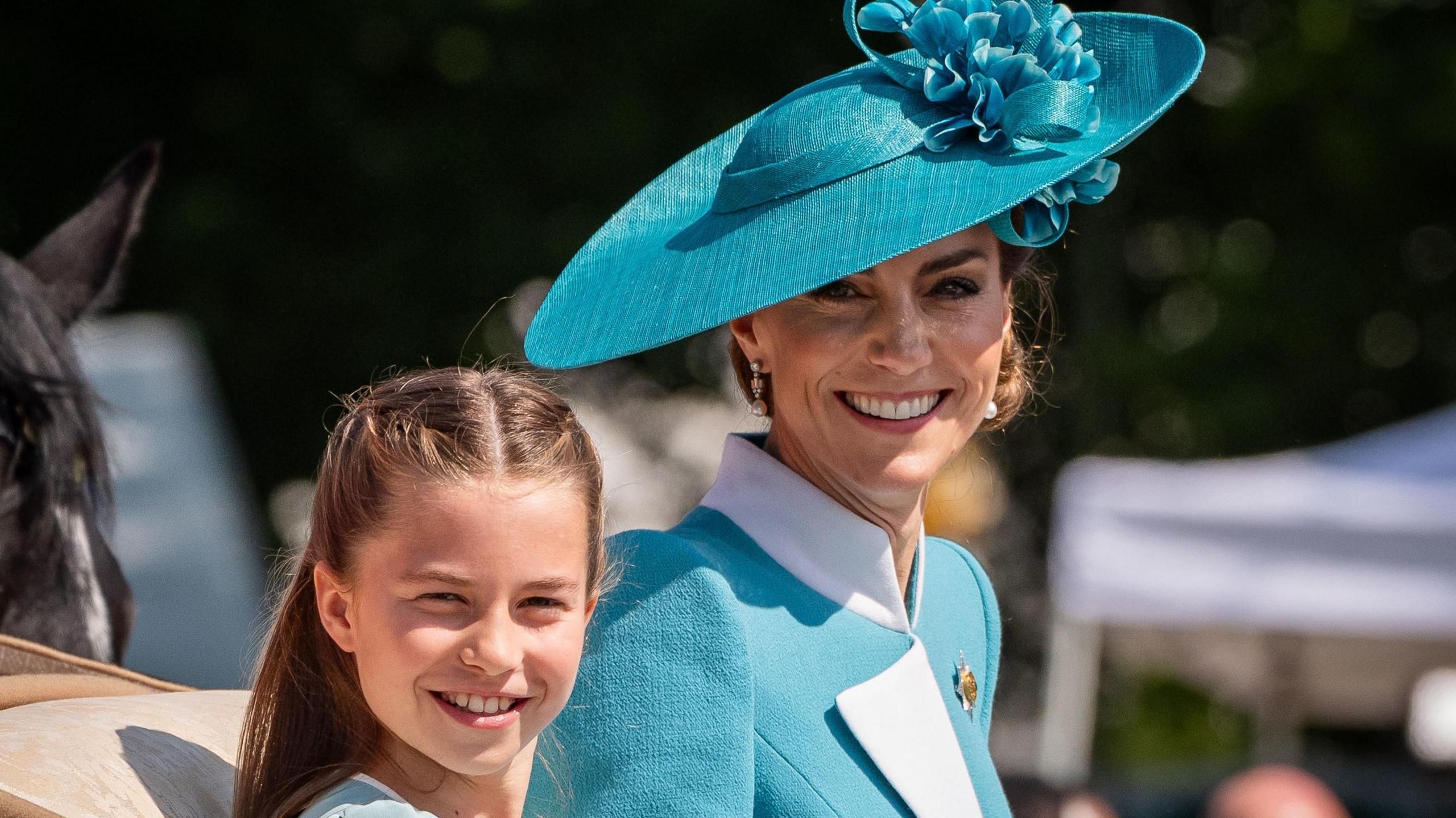 Catherine, Princess of Wales and Princess Charlotte in teal dresses, smiling from a carriage during Trooping of the Colour