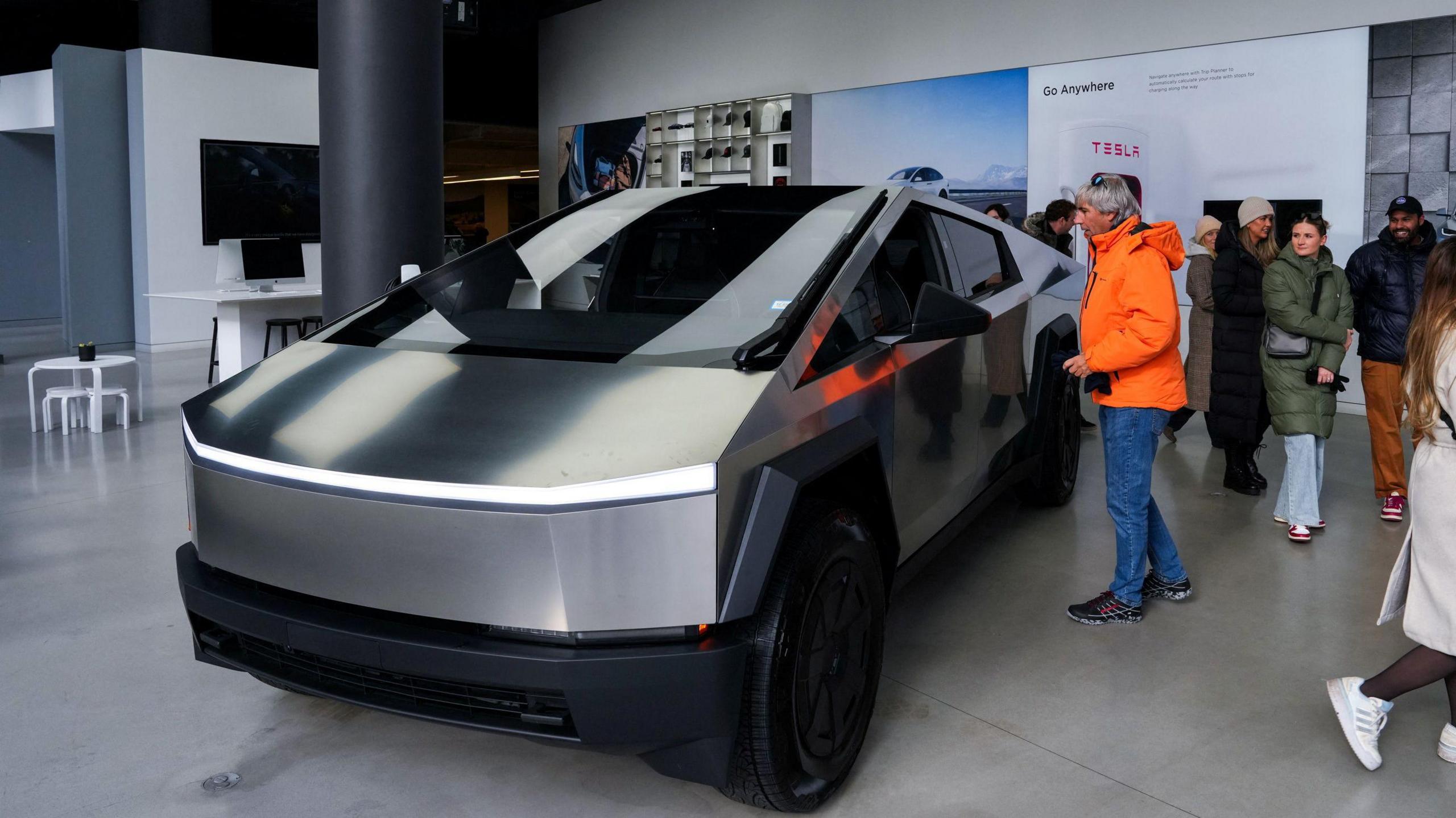 A silver Tesla Cybertruck is viewed by a crowd of people at a showroom