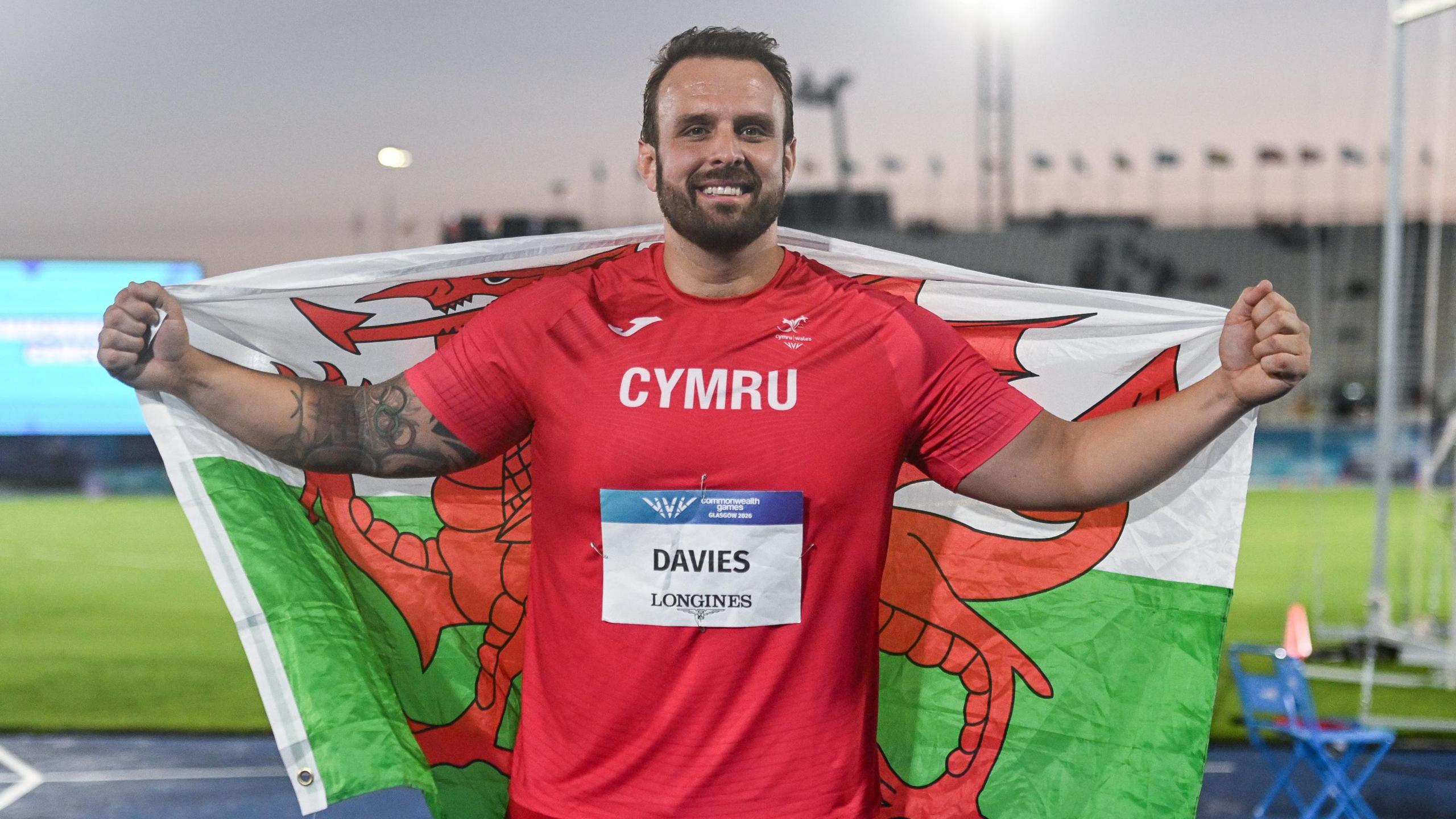 Aled Davies, who was the Team Wales captain when the Commonwealth Games was previously held in Glasgow in 2014, holds the Welsh flag around his back