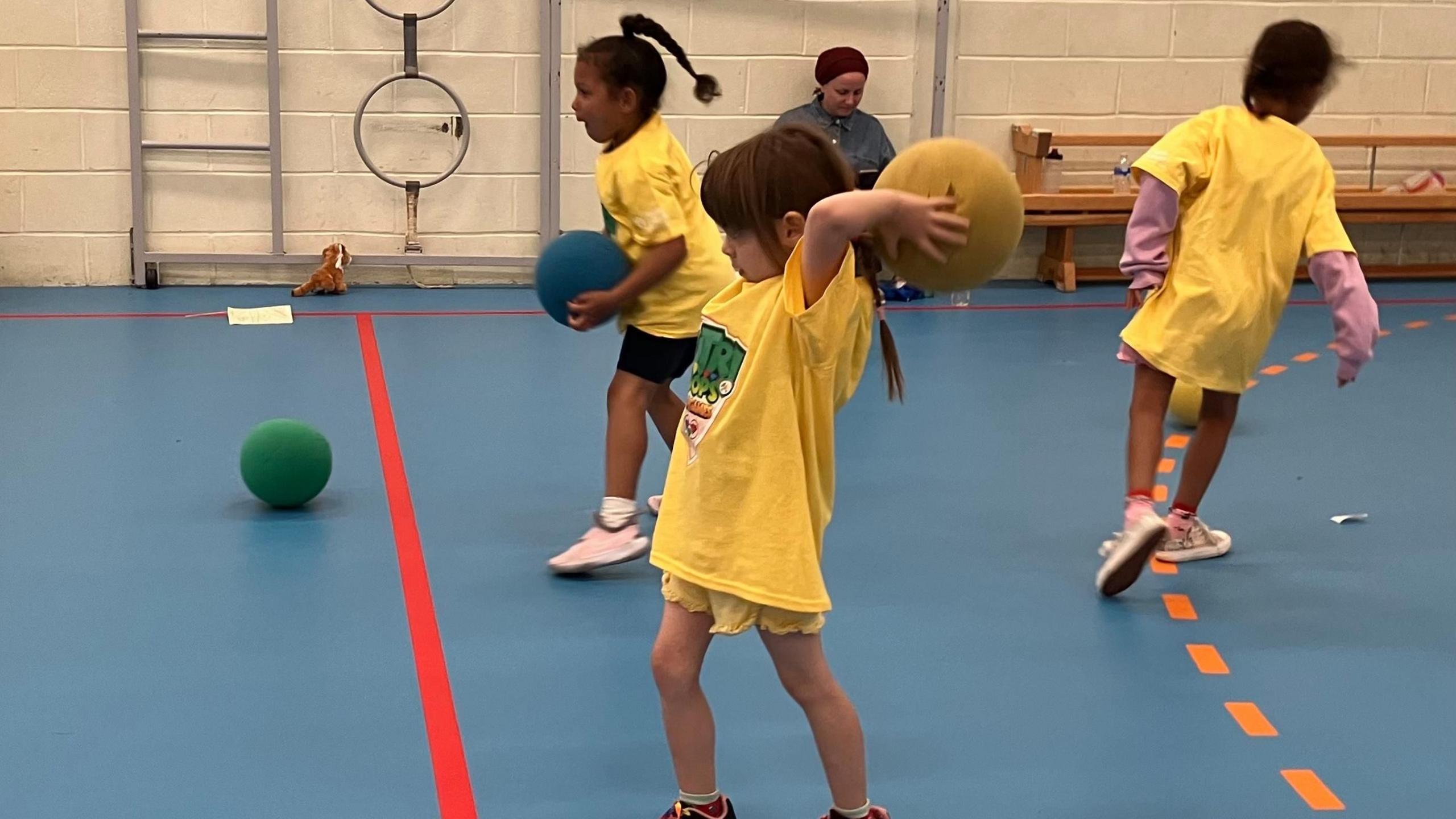 Children in yellow t shirts throwing sponge balls in a  sports hall