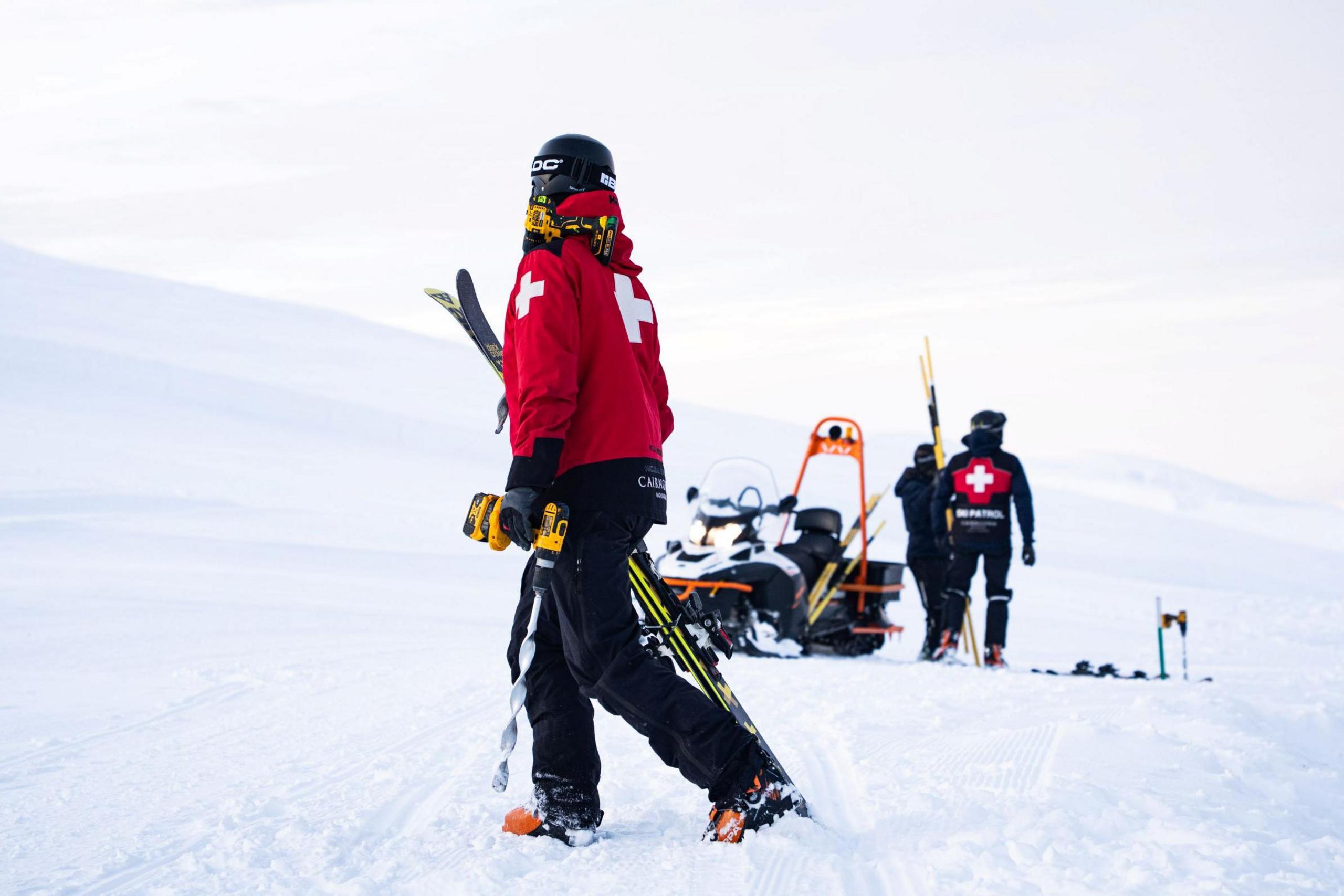 Ski patrollers in red and black clothing in the snow.