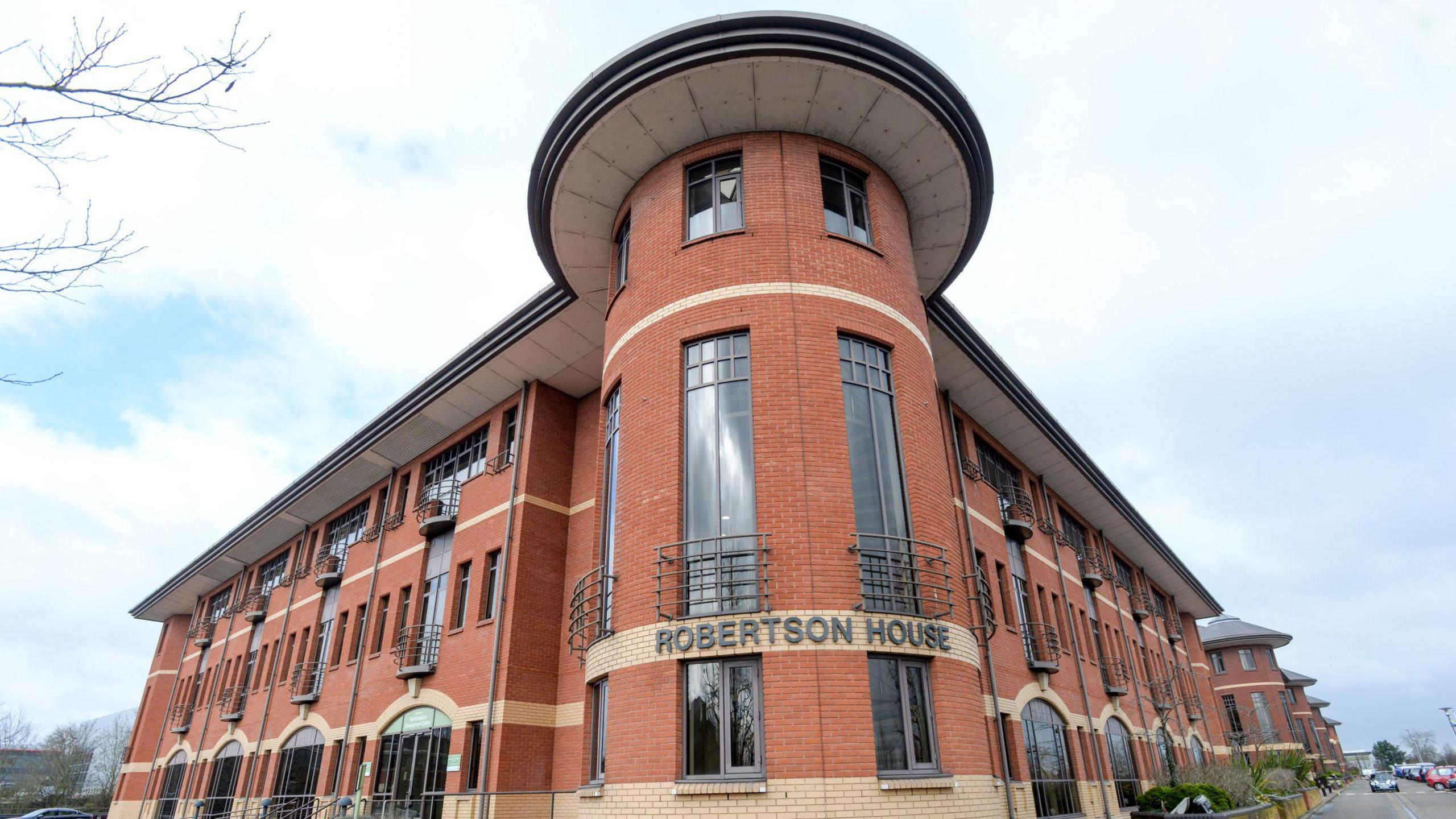 A picture of Robertson House in Stevenage, which is now the main base for Hertfordshire County Council. It is a mainly red brick building, on three floors, and large windows.