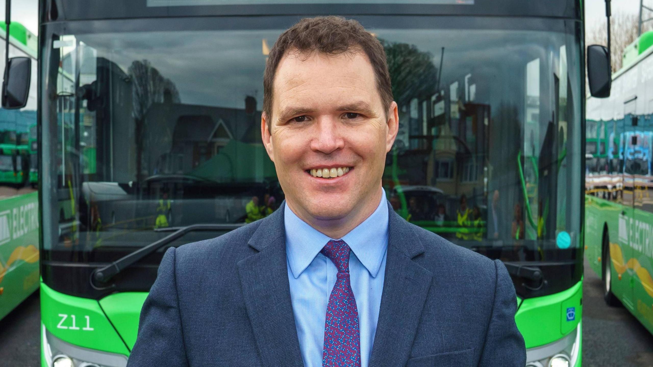 Llyn yn dangos dyn yn gwenu i'r camera mewn siwt a thei.