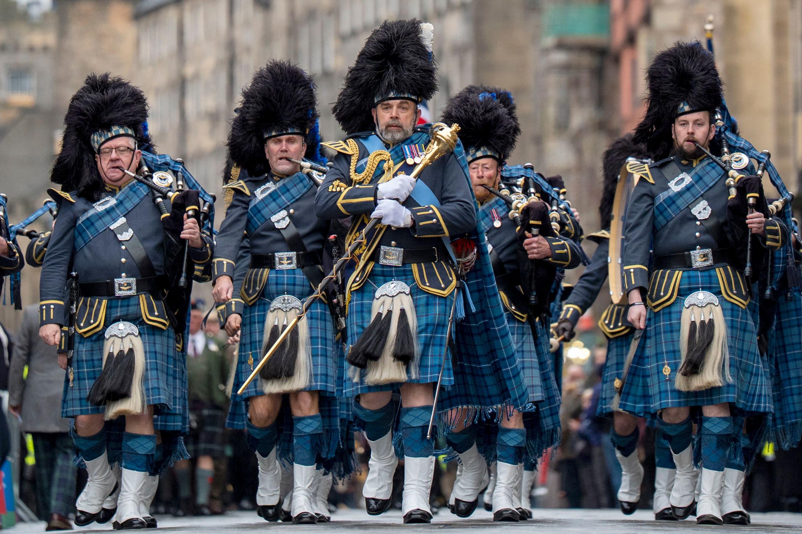 A row of men in blue tartan kilts and plaids playing bagpipes