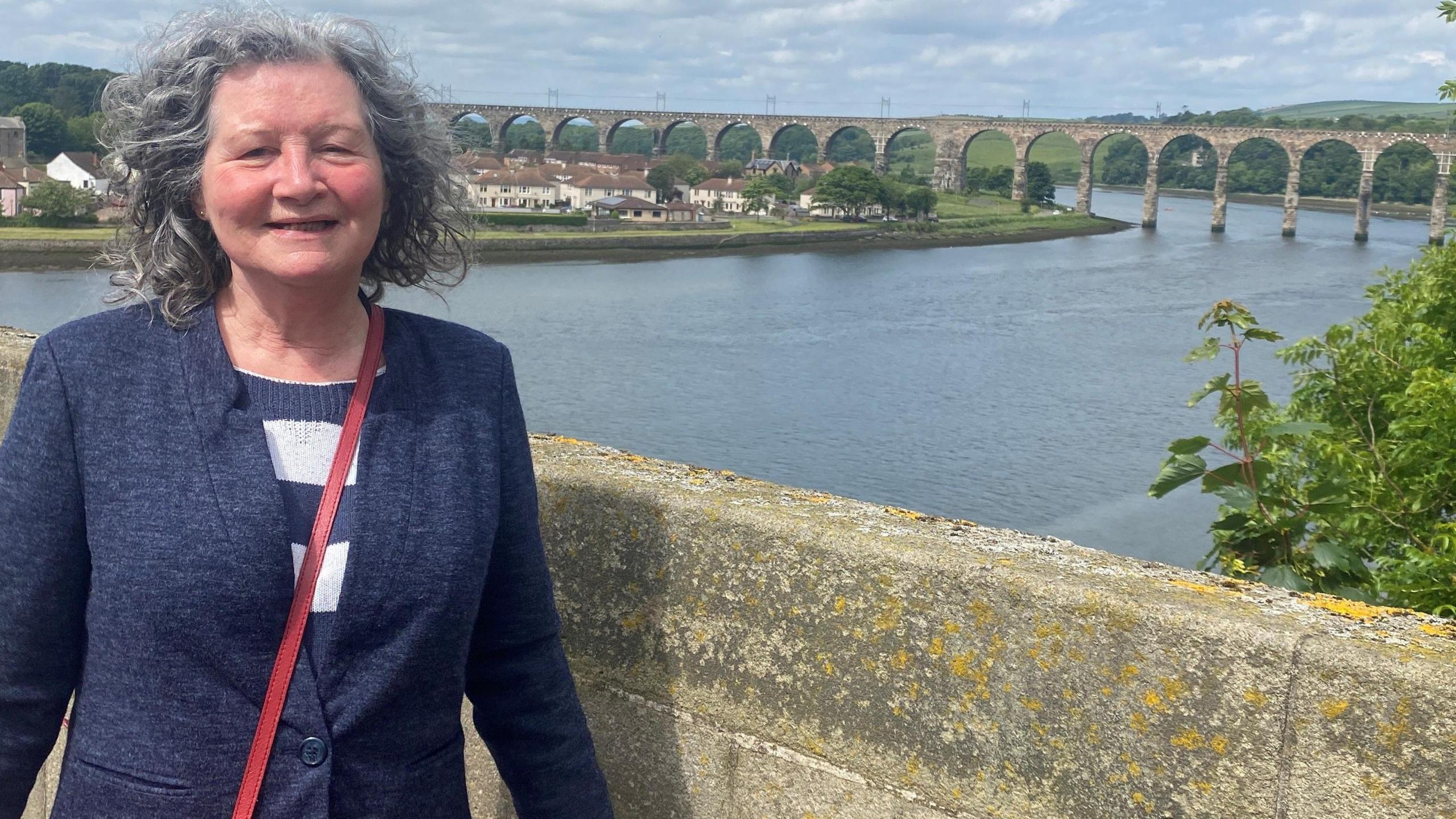 Diane Youll standing on a bridge with the main railway bridge over the Tweed in the background