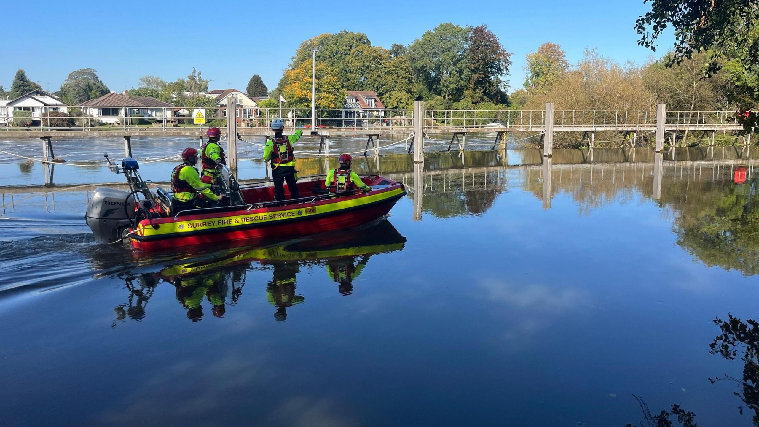 A red Surrey Fire and Rescue service boat heads out on to the River Thames, with four crew members in hi-vis.