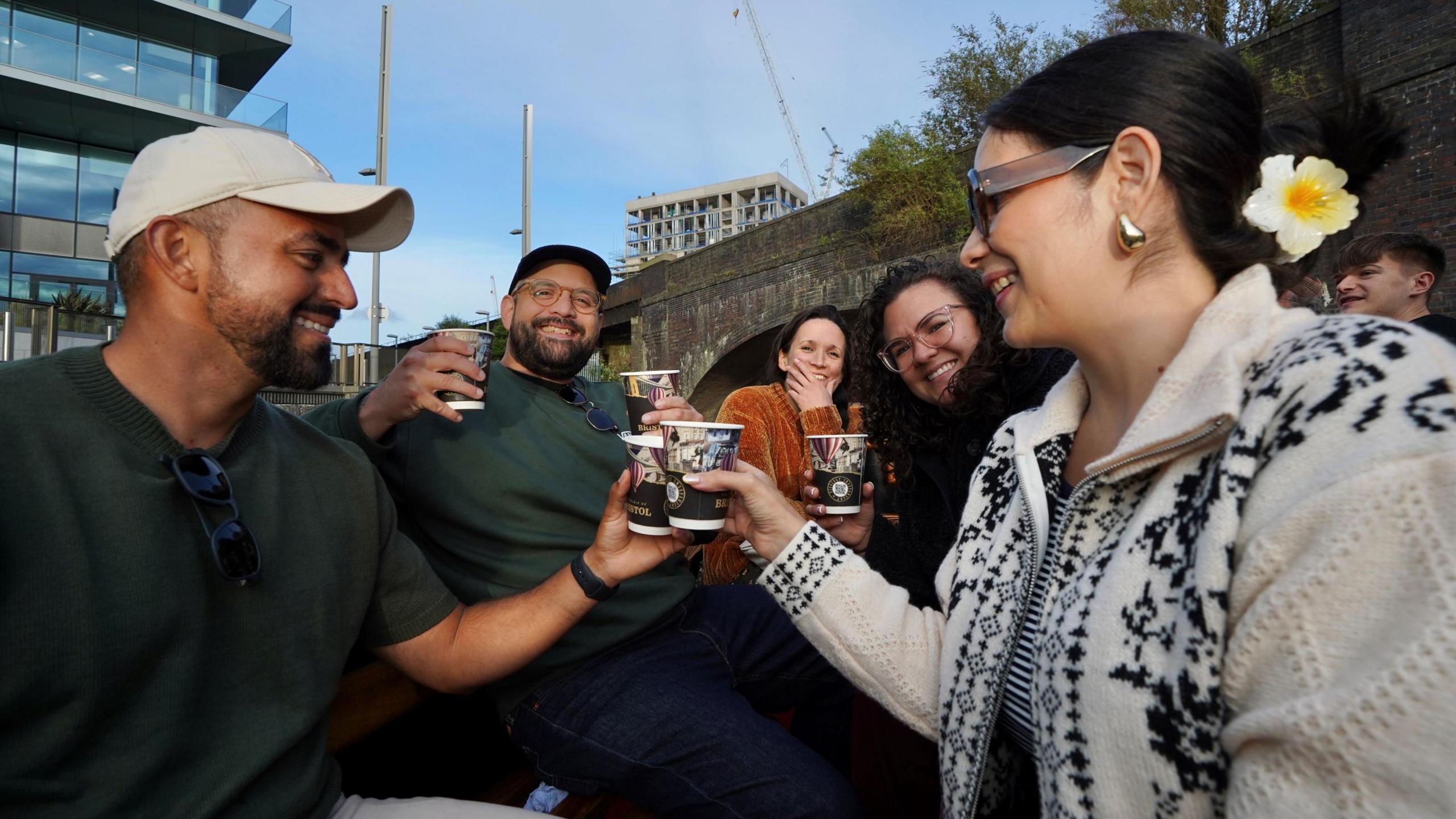 A group of people 'cheers' each other with Spirit of Bristol gin drinks on a special cruise around the harbourside