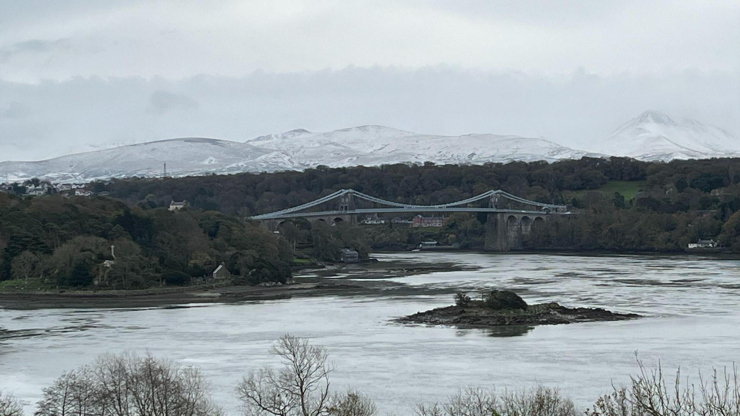 Menai Bridge and Menai Strait water with mountains in the background covered in snow