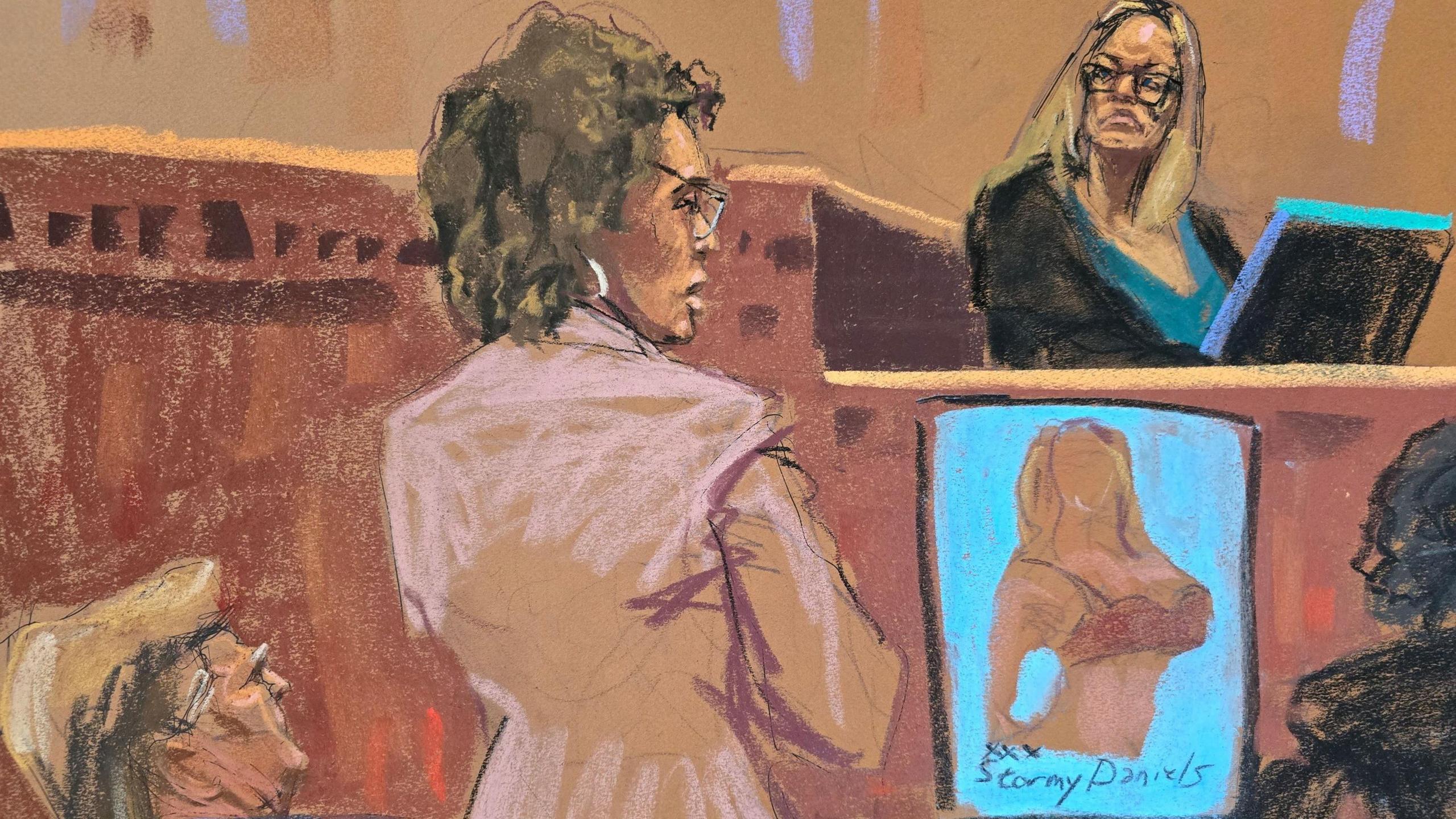 Court sketch shows Stormy Daniels on the witness stand, with a poster of her wearing a bra on show as a court exhibit. Trump's lawyer is standing up in front of her, and Trump can be seen looking up towards the witness stand