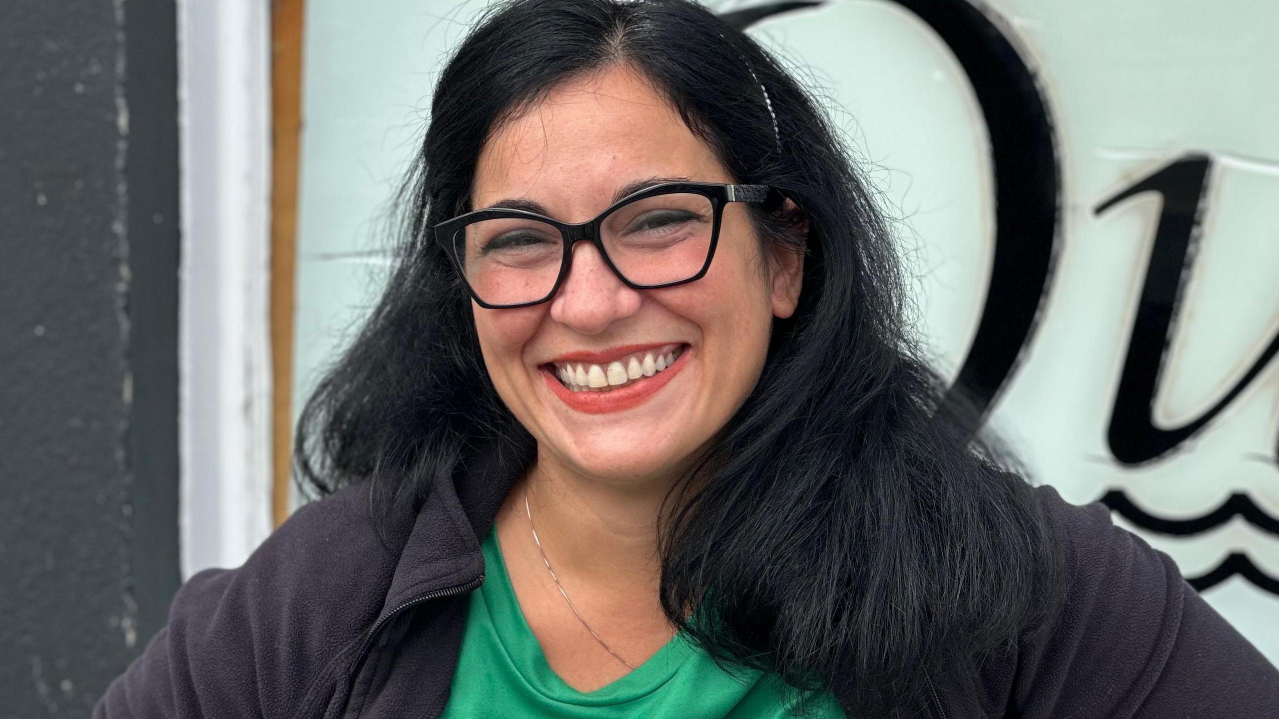 Matilde Liso, who has long dark hair and is wearing black rimmed glasses and a black top over a green T-shirt. She is smiling.
