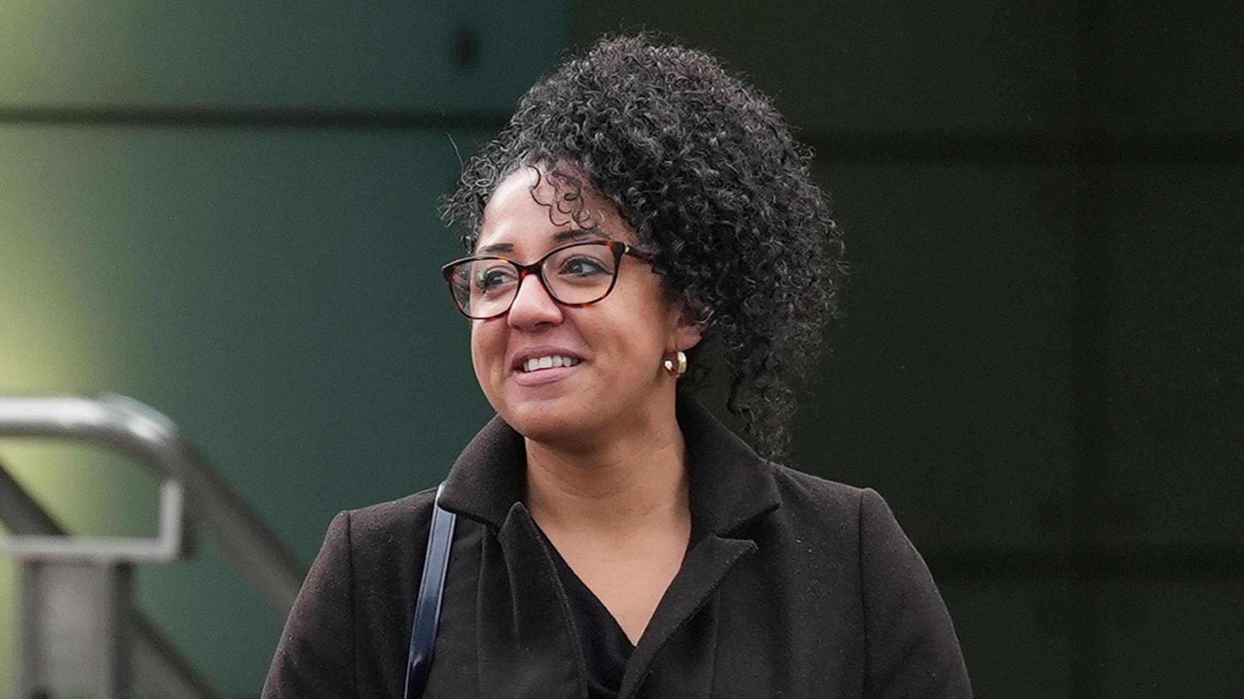 A photo of PC Korell outside the police building where the misconduct panel took place. She is wearing glasses, a dark coat and a black dress and a handbag strap is visible on her right shoulder.