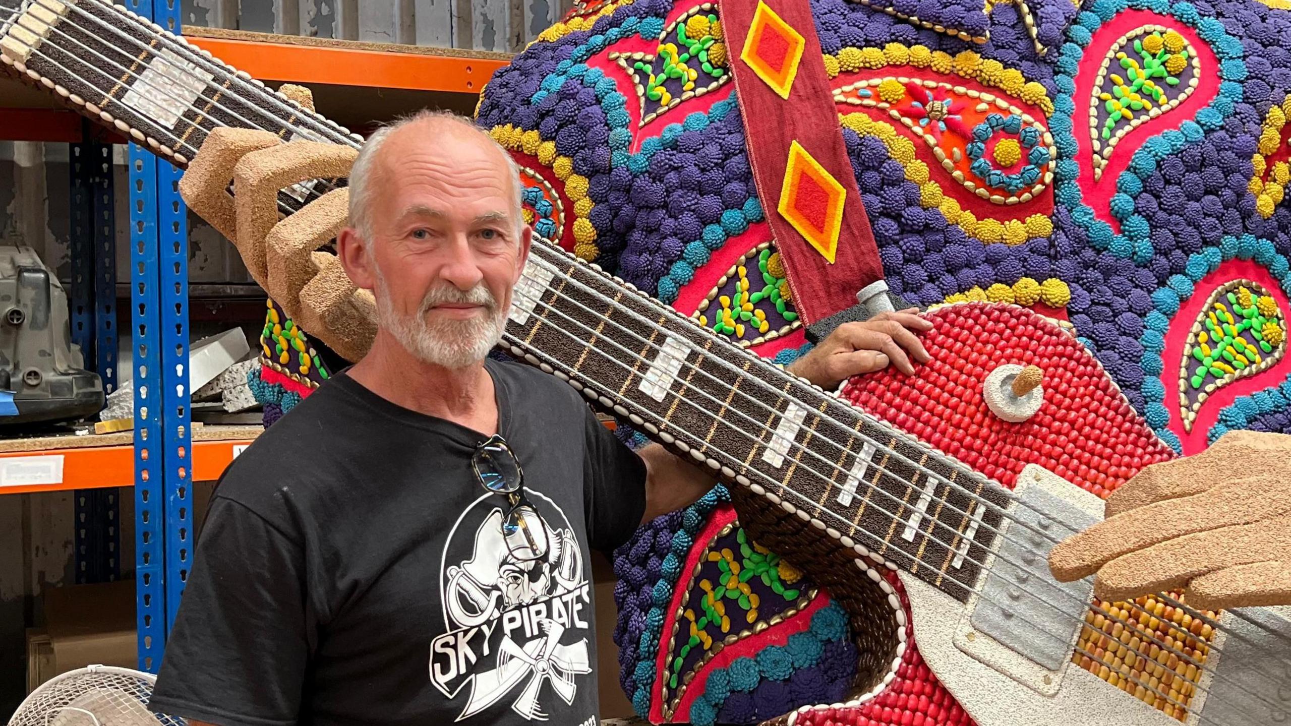 Nick looking at the camera next to part of the Grouville float - it's a giant man with a guitar made of different colours of lentils