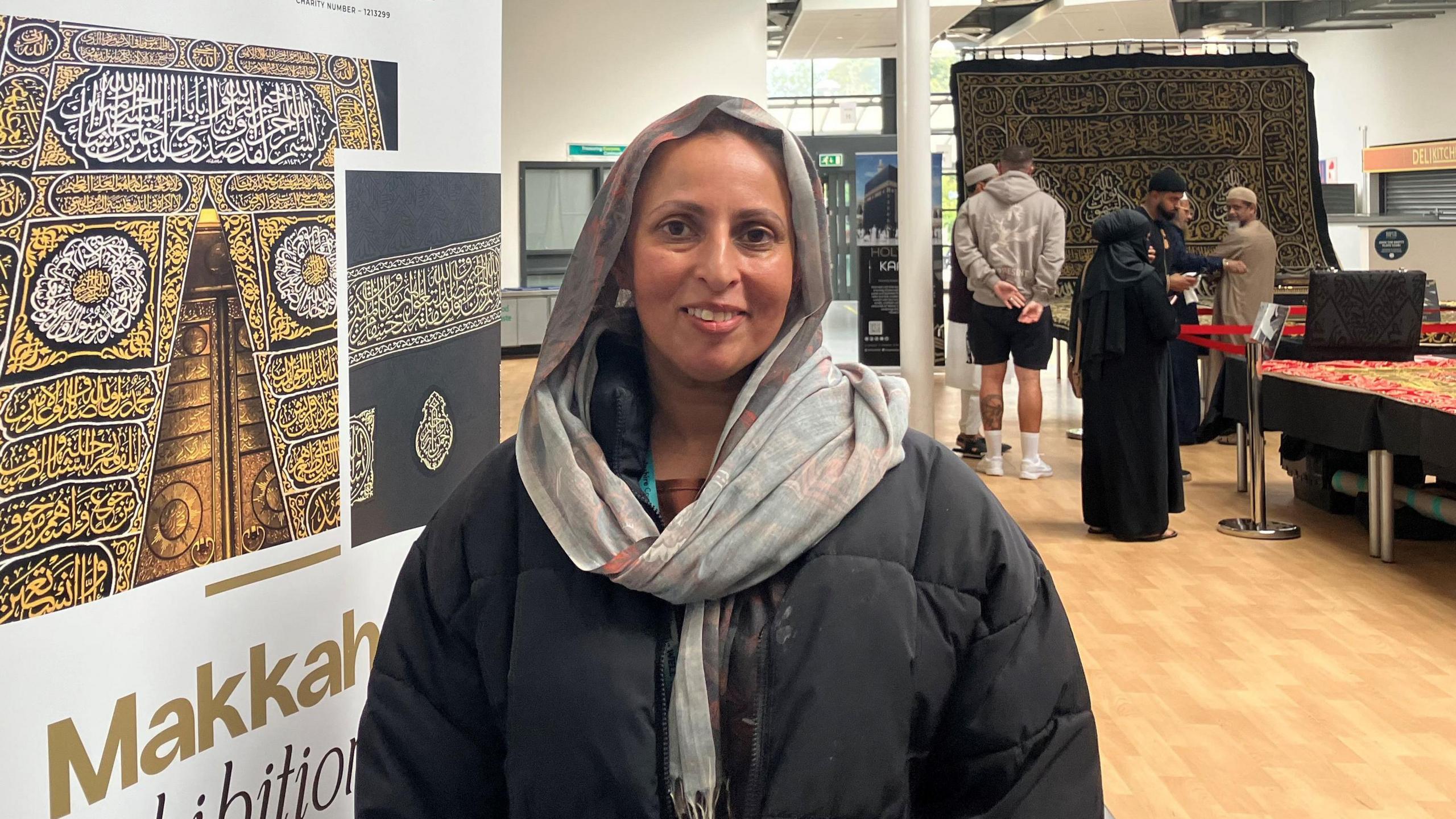 A woman with a headscarf and a black jacket with people behind looking at rare Islamic artefacts in a school hall.
