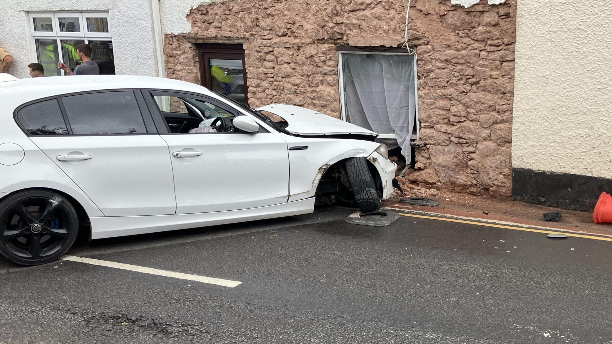 The damaged white Volkswagen in front of a home with a hole in it