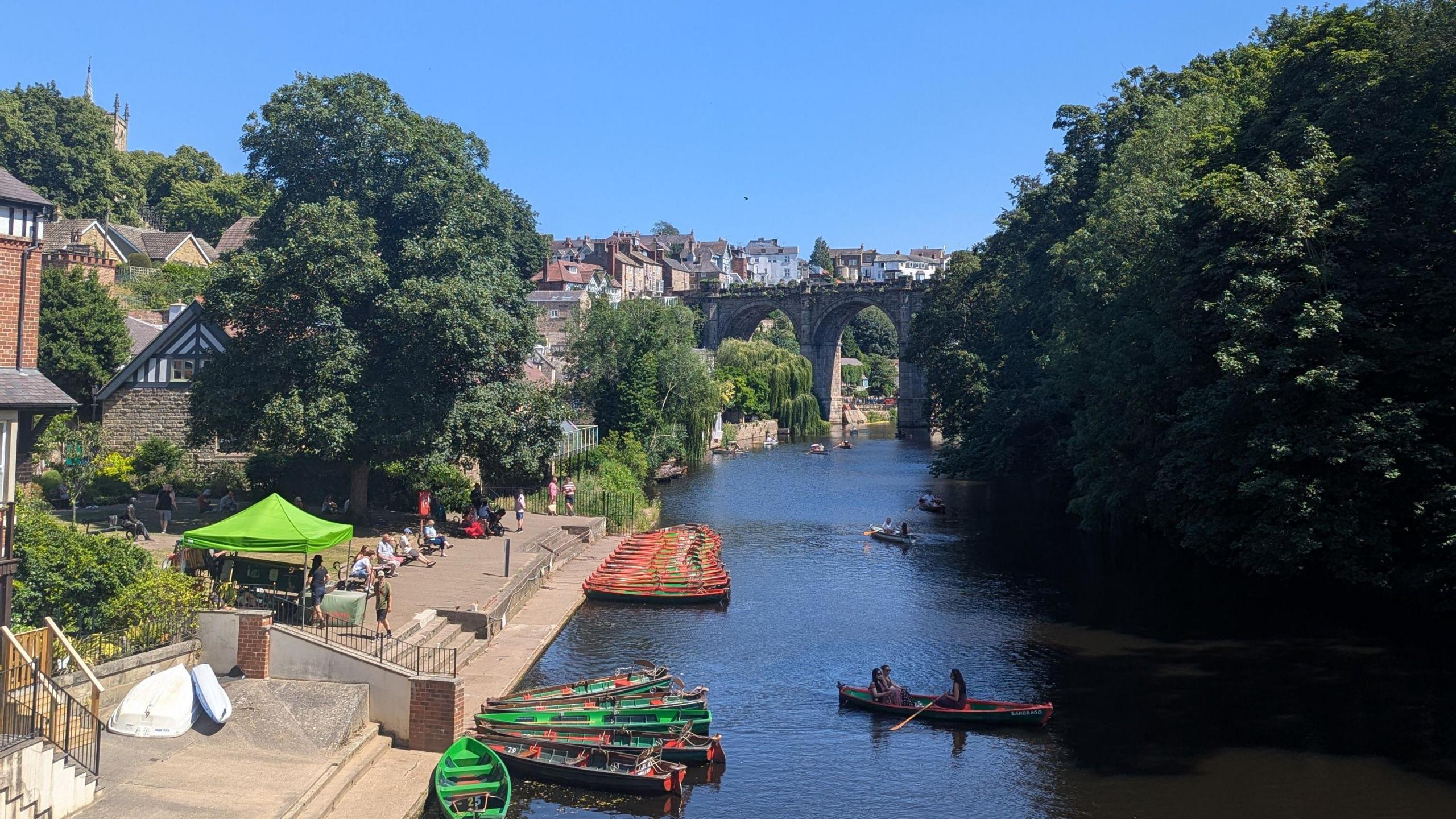 A view of Knaresborough Viaduct standing over the River Nidd. People are rowing in the river.