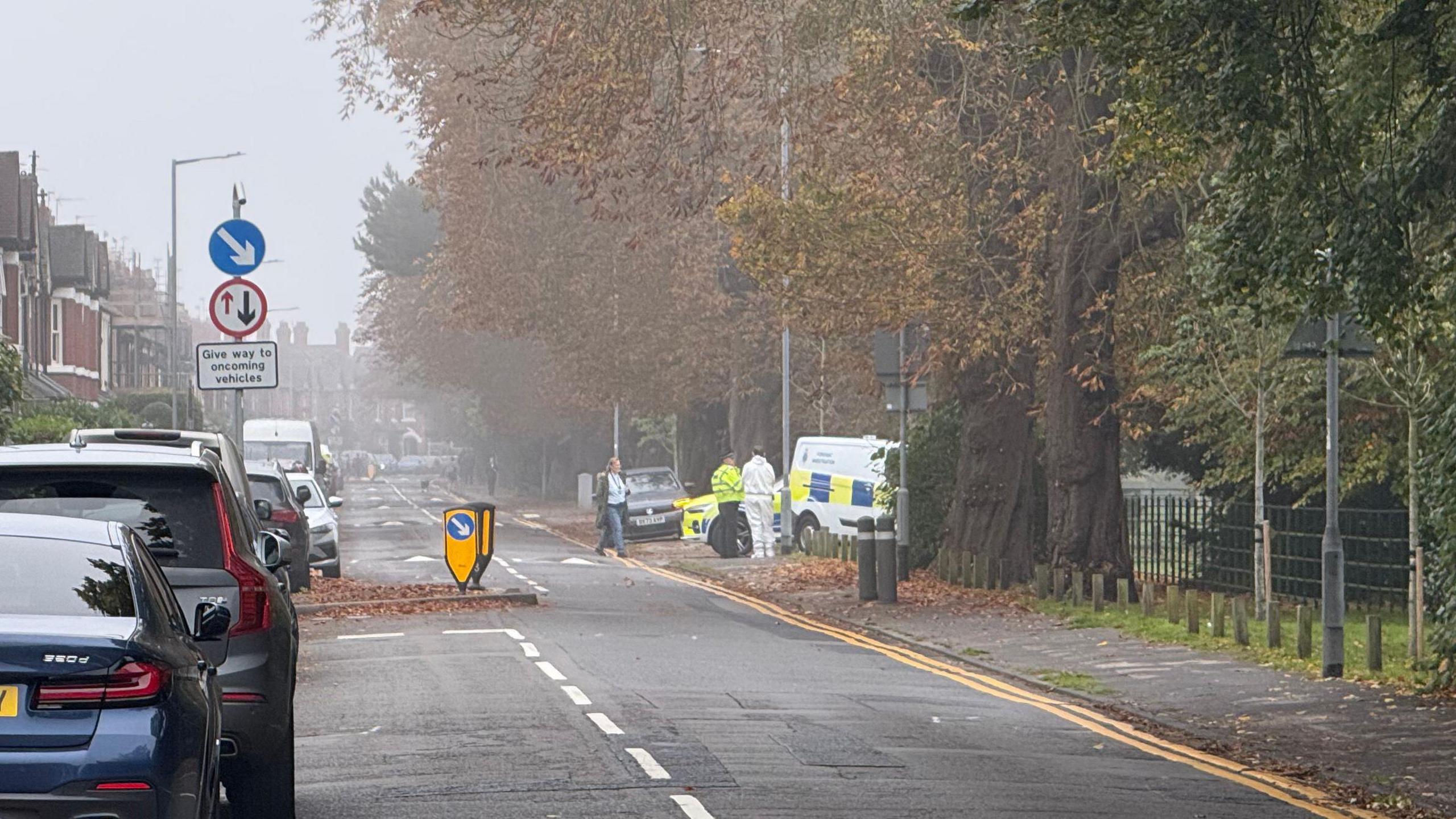 Corporation Street in Stafford, with trees lining each side of the road. There are cars lining the left hand side of the road, with emergency service vehicles and workers visible on the left hand side. 