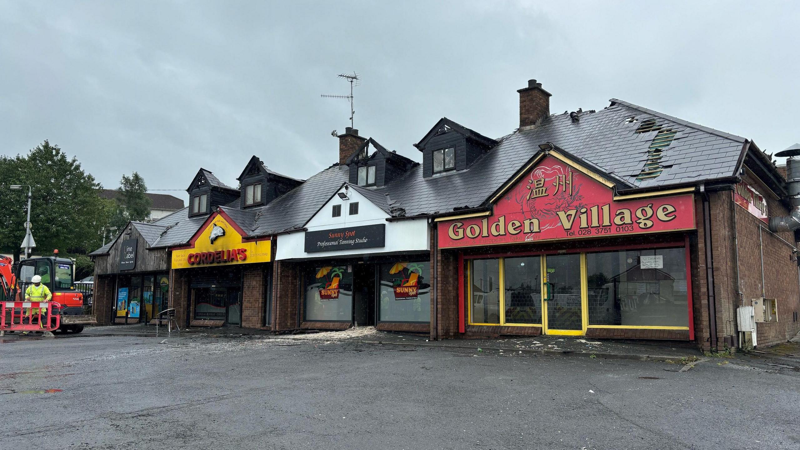 A wide shot of the whole unit damaged by fire showing Cordelia's chip shop, an off licence, tanning salon and Chinese takeaway