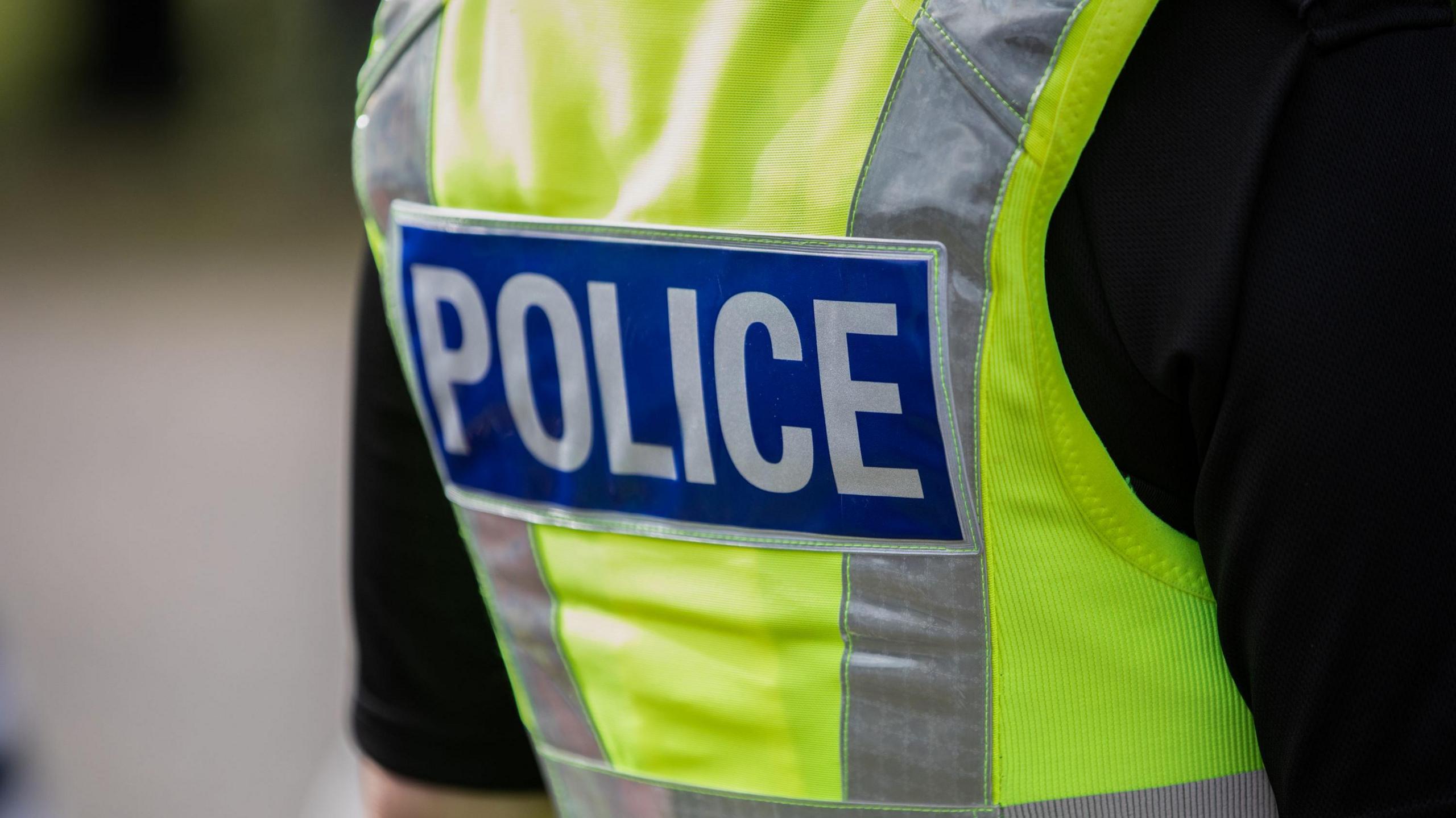 Back of a police officer wearing a black t-shirt and hi-vis vest.