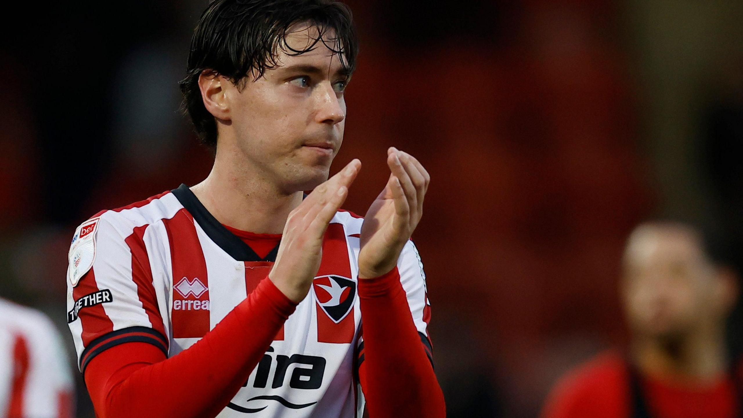 Isaac Hutchinson applauds the Cheltenham fans at the end of a match in the team's red and white home jersey