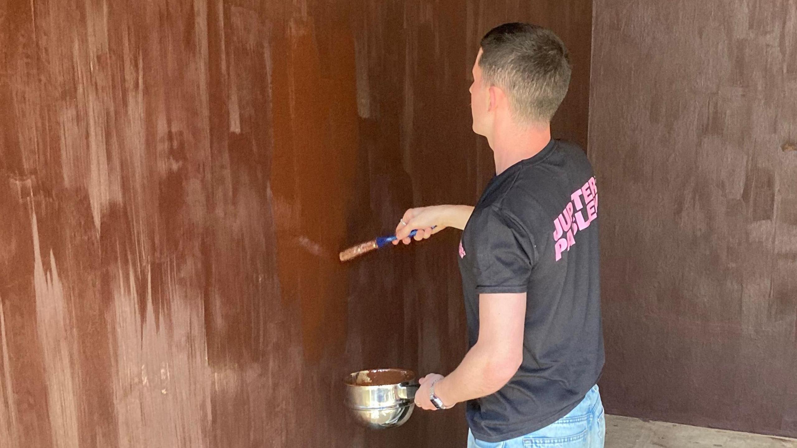 A person paints a wall in chocolate coloured paint