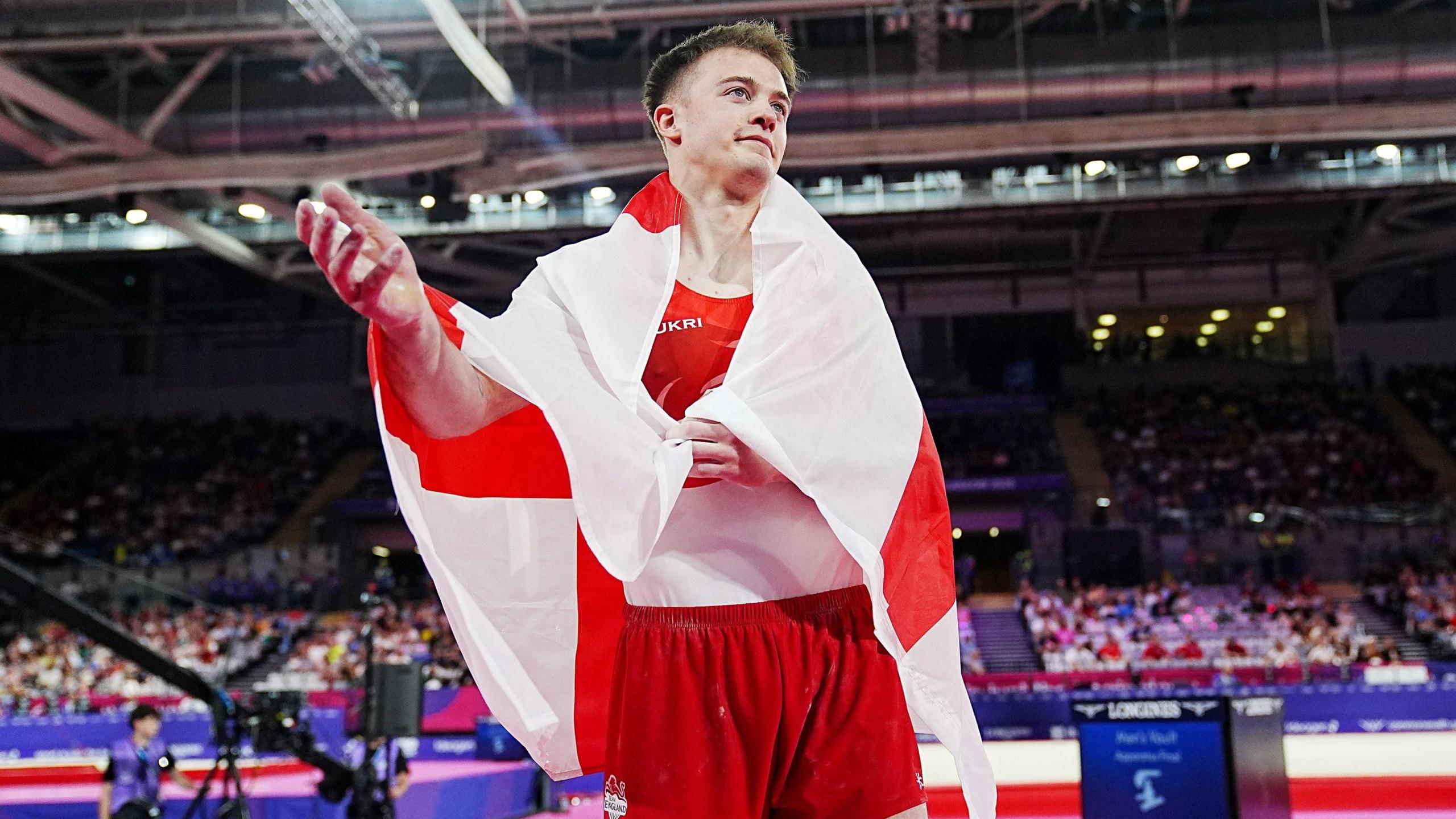 Luke Whitehouse gesturing to the crowd wrapped in an England flag after winning silver on the vault at the Commonwealth Games in Glasgow