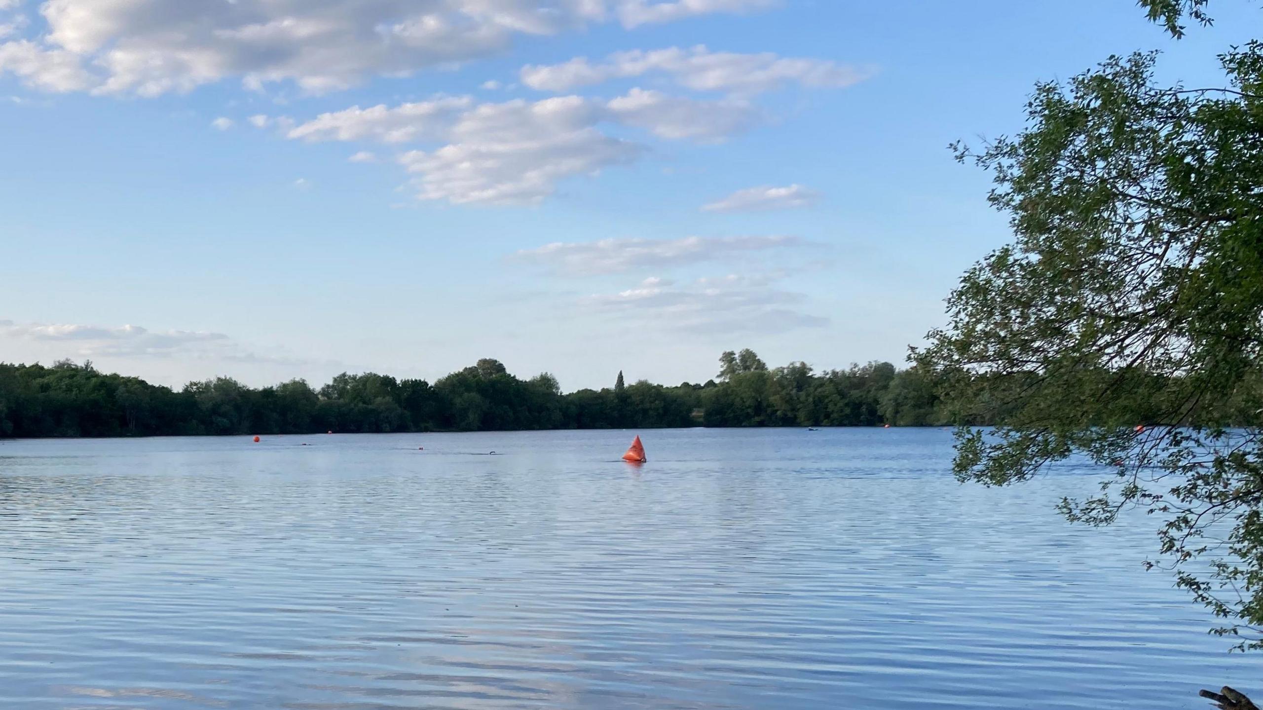 A general view of the lake, which is large and lined with trees. It is pictured on a sunny day.