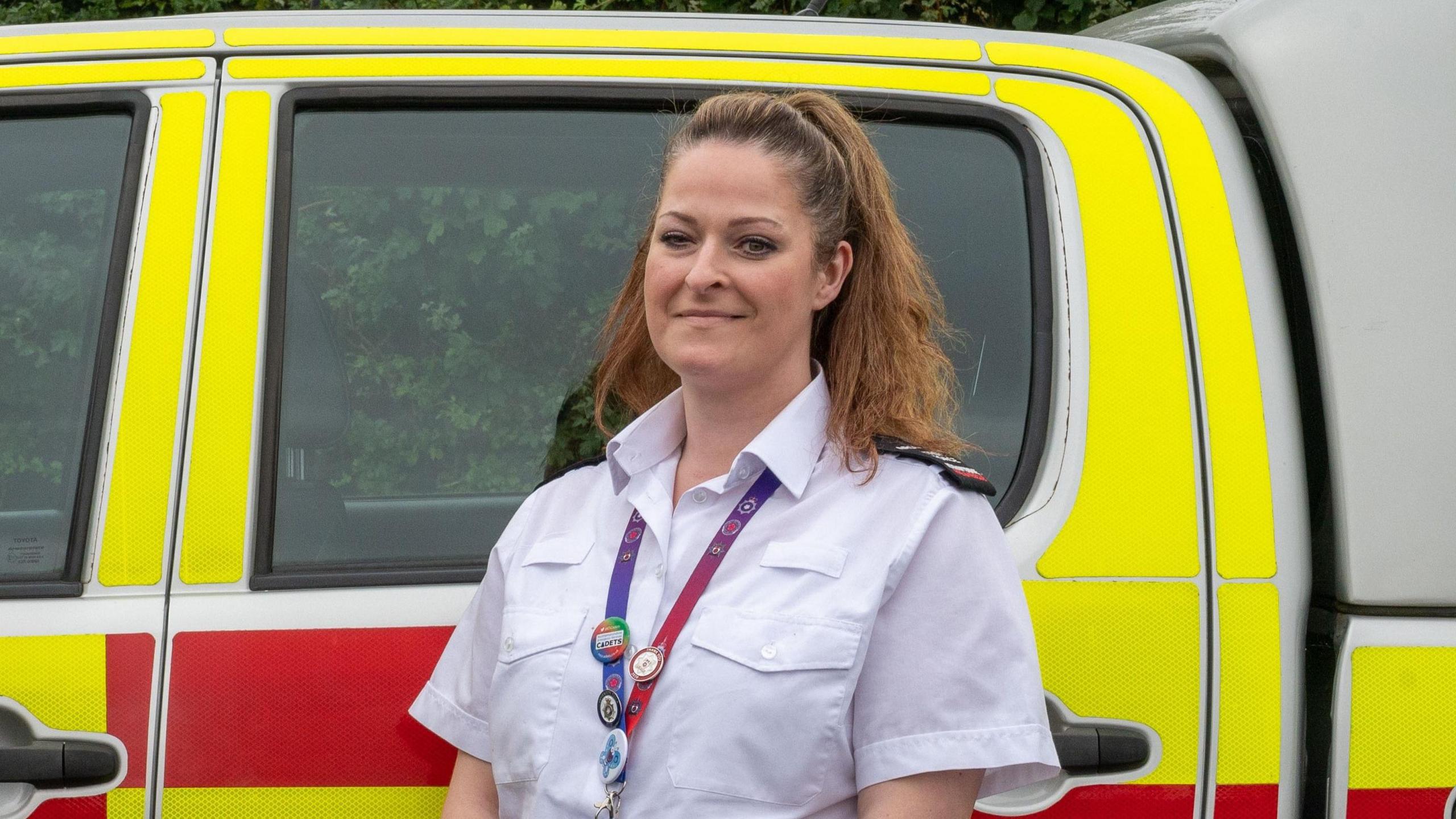 Kelly Crockett with long brown hair wearing a lanyard and standing in front of a yellow and red fire service vehicle