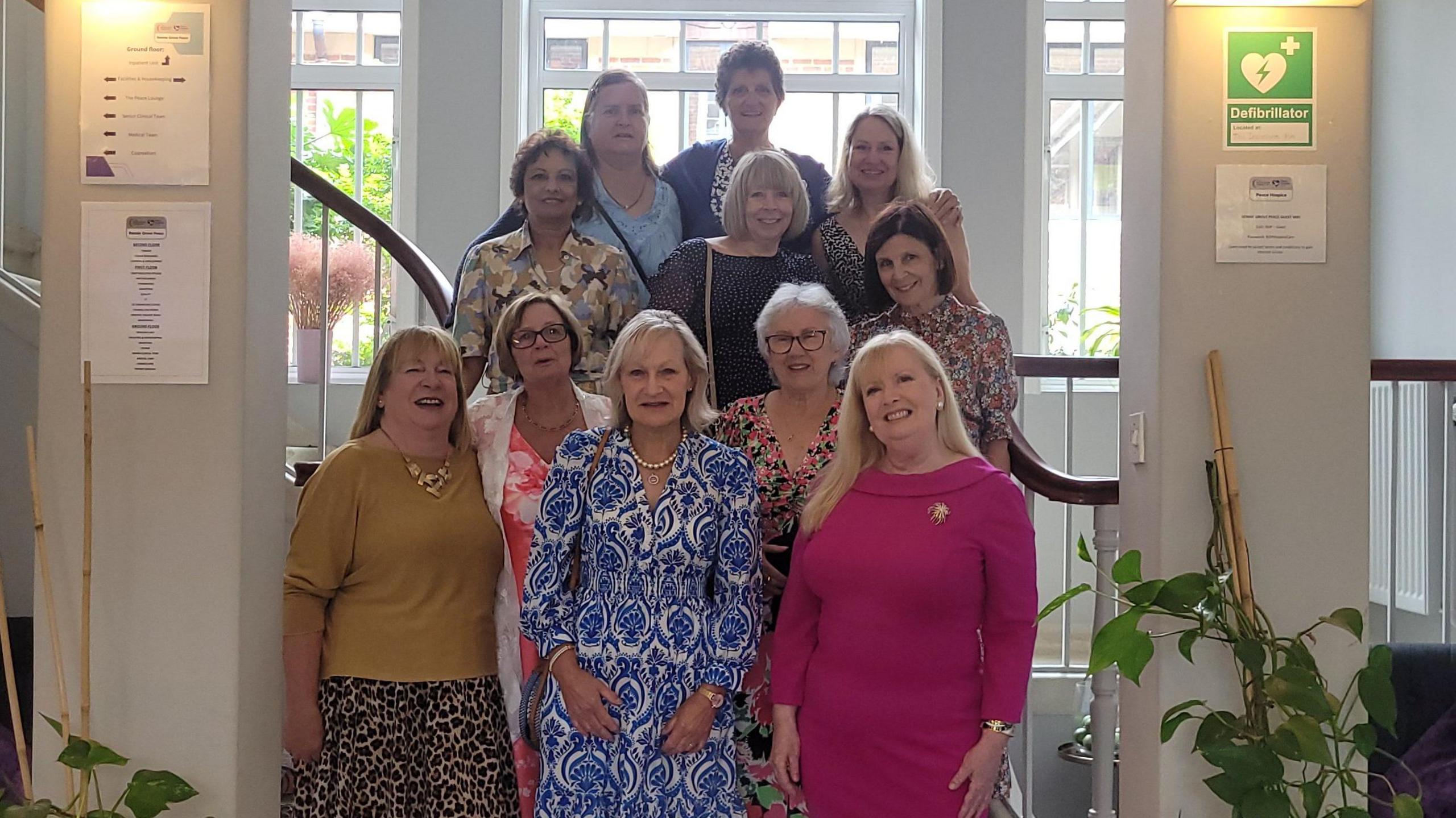 Eleven women pose for a photo at the bottom of some stairs to mark 50 years since they began their nurse training