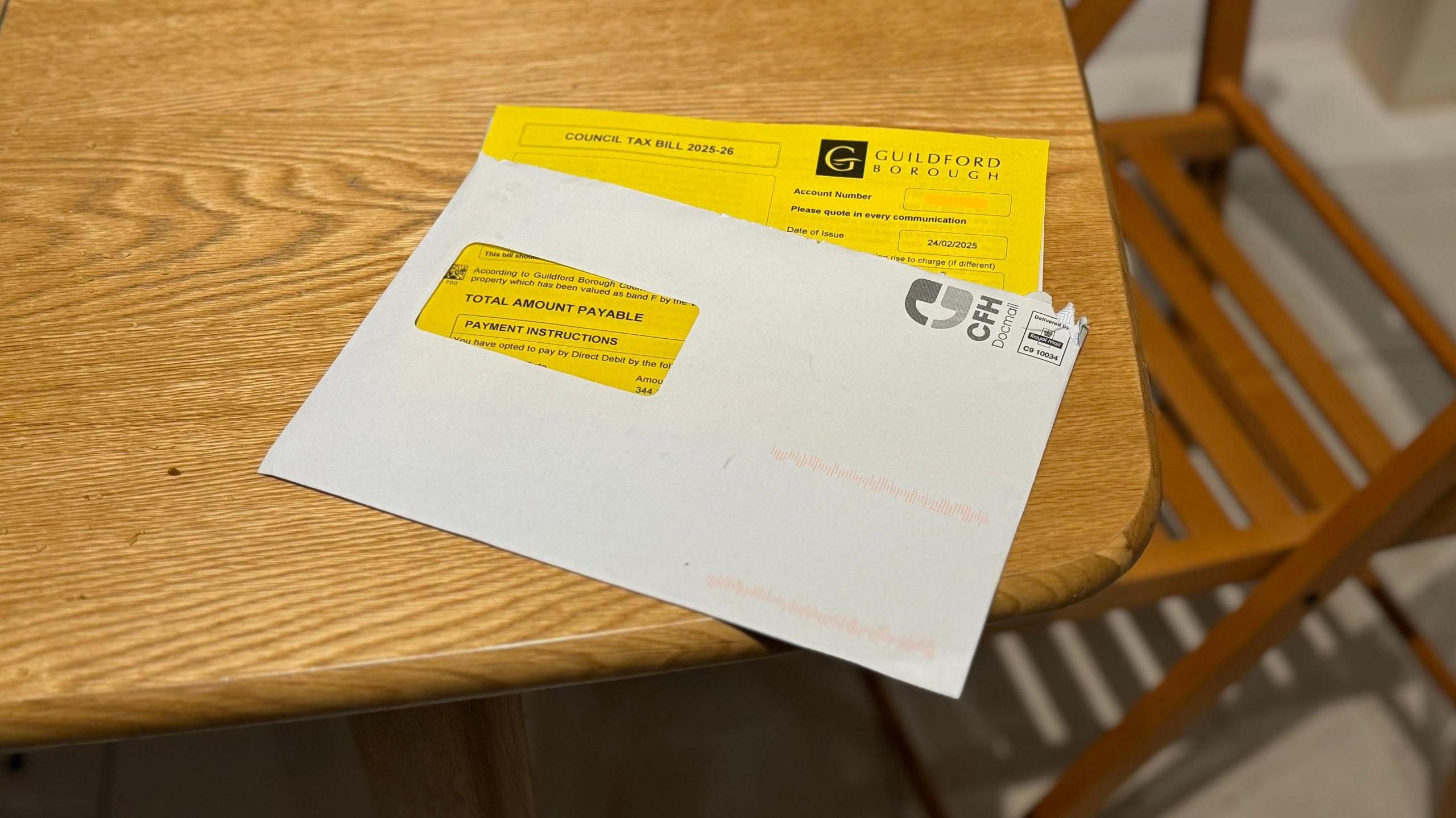 A Guildford Borough Council council tax bill, on a kitchen table. It is halfway out of the envelope. There is a chair in the background.