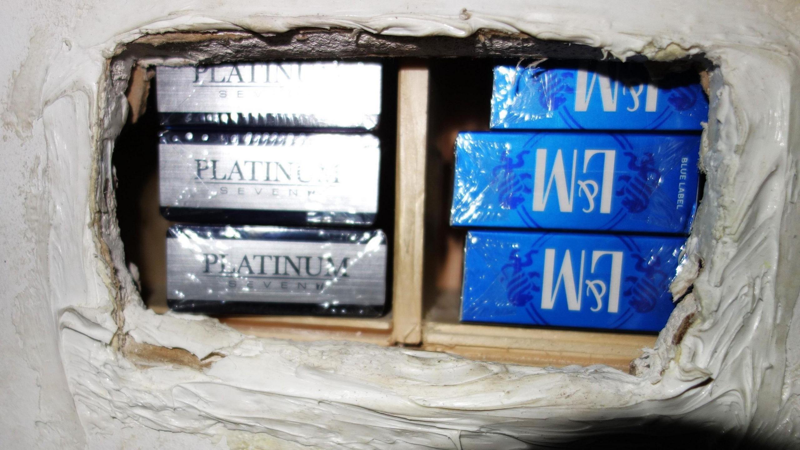 A hole in the wall holding two rows of cigarettes in blue and silver packages