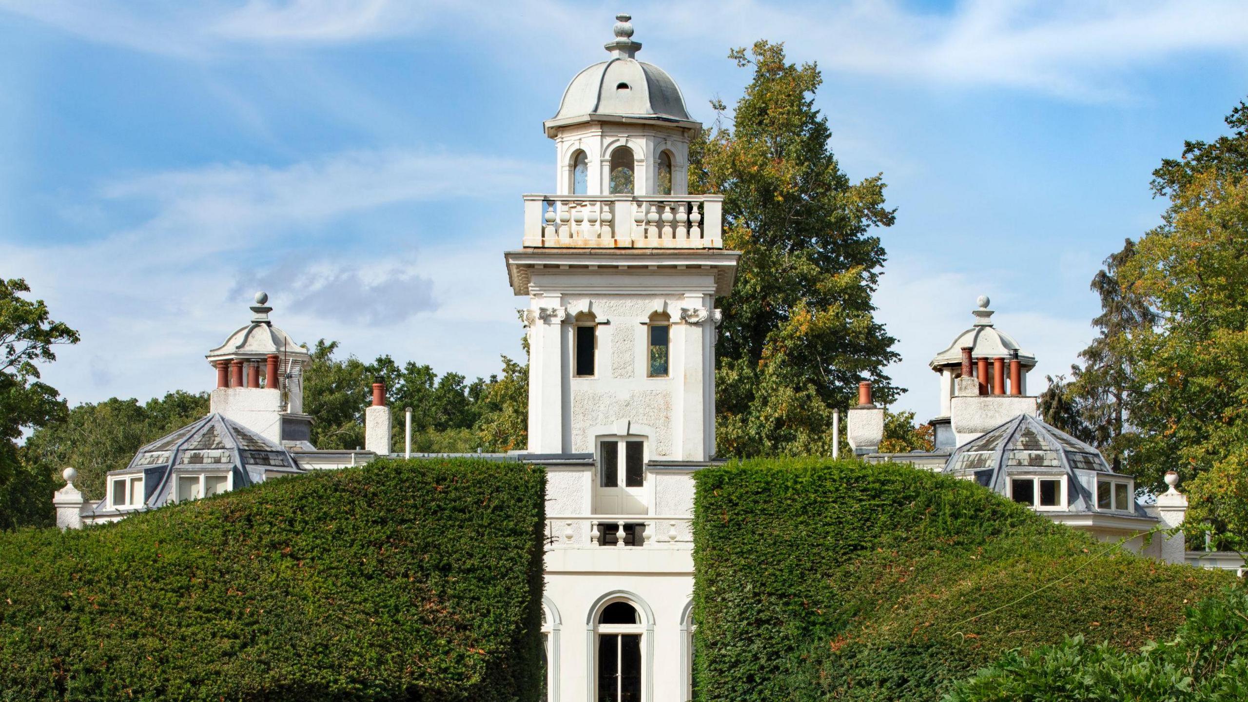 A white tower surrounded by a trimmed hedge.