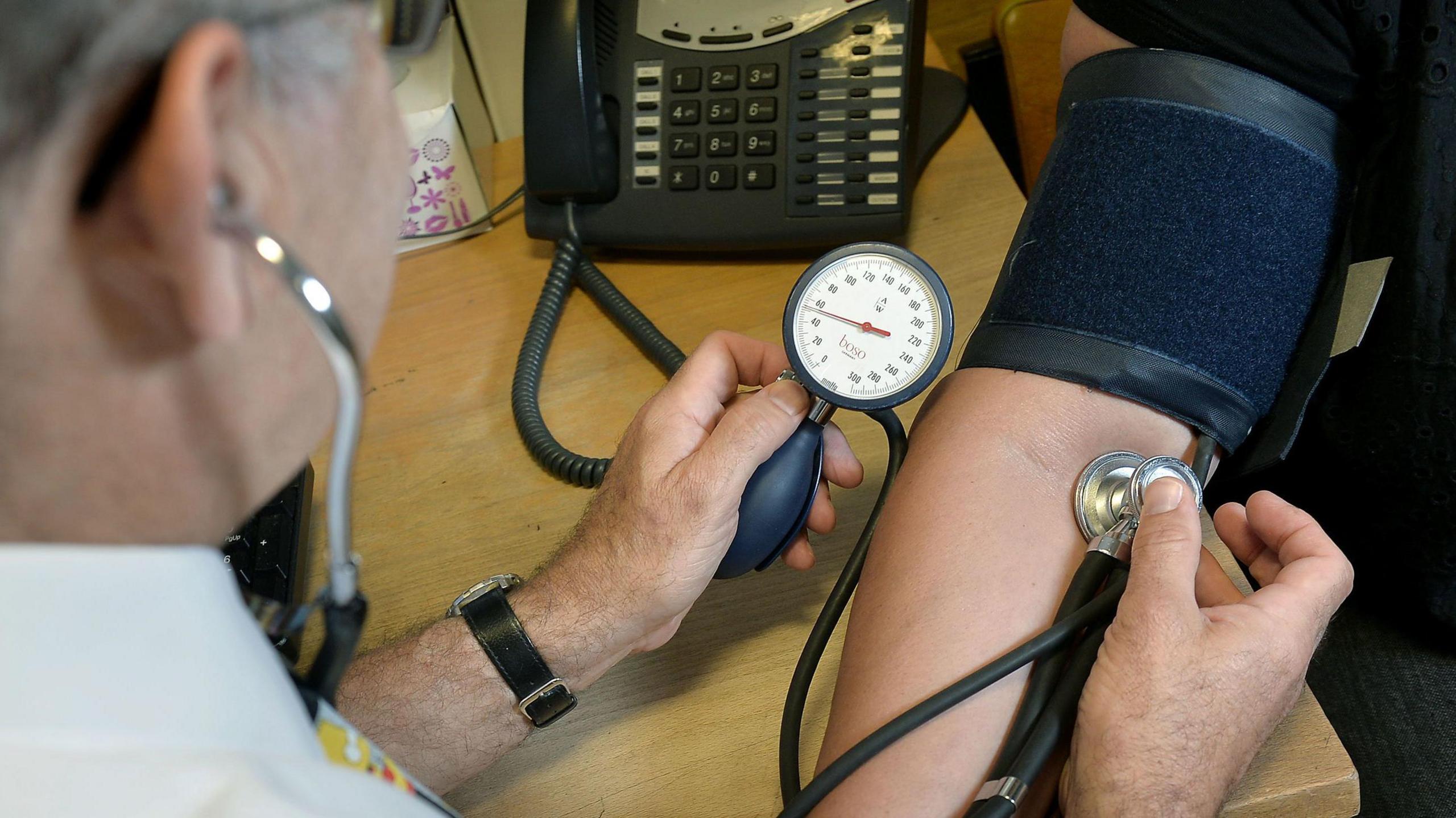 A doctor is using medical equipment including a blood monitor cuff to monitor someone's blood pressure. 