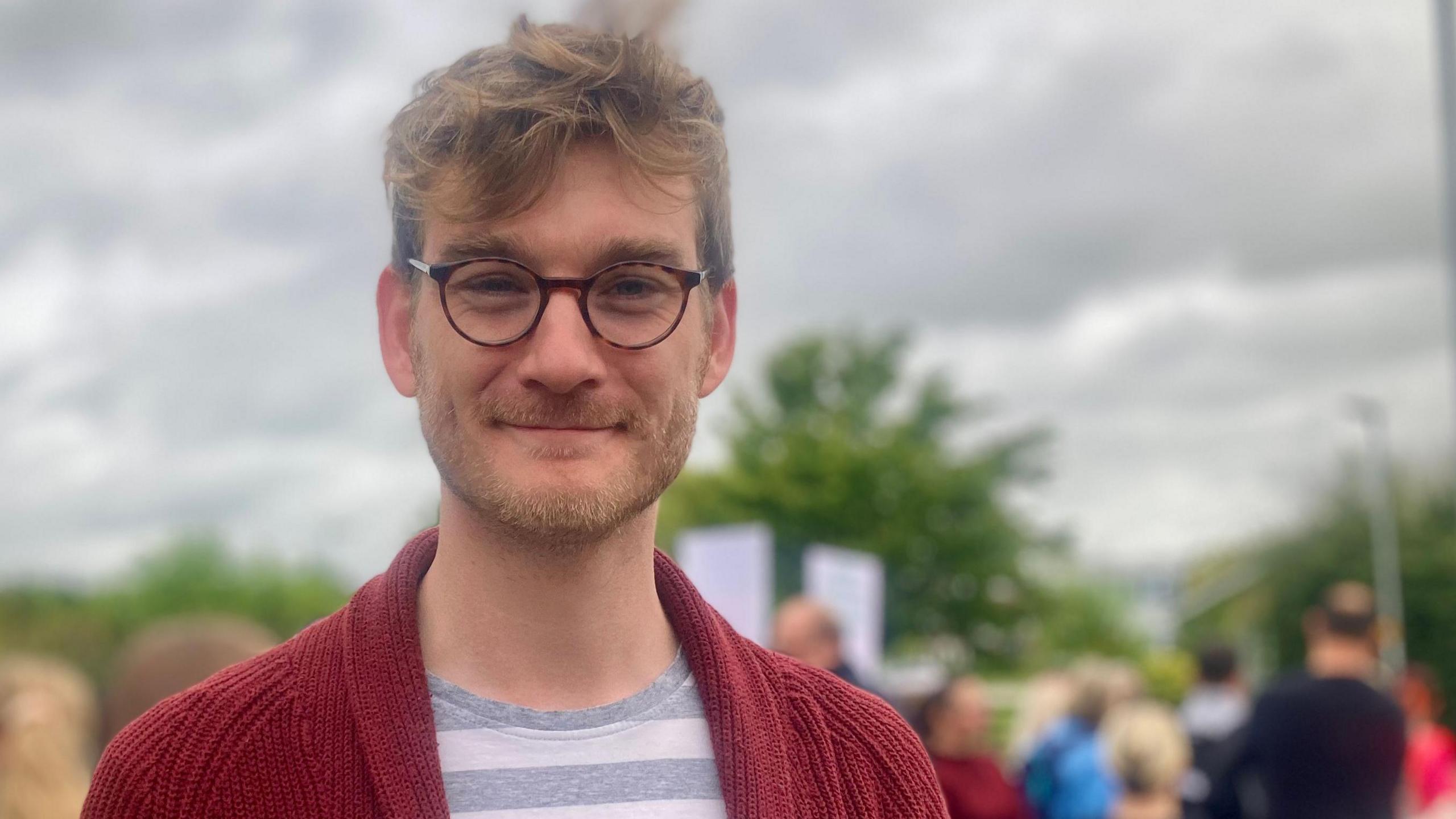 Sam Blake smiling at the camera, while parents and teachers wave placards in the background