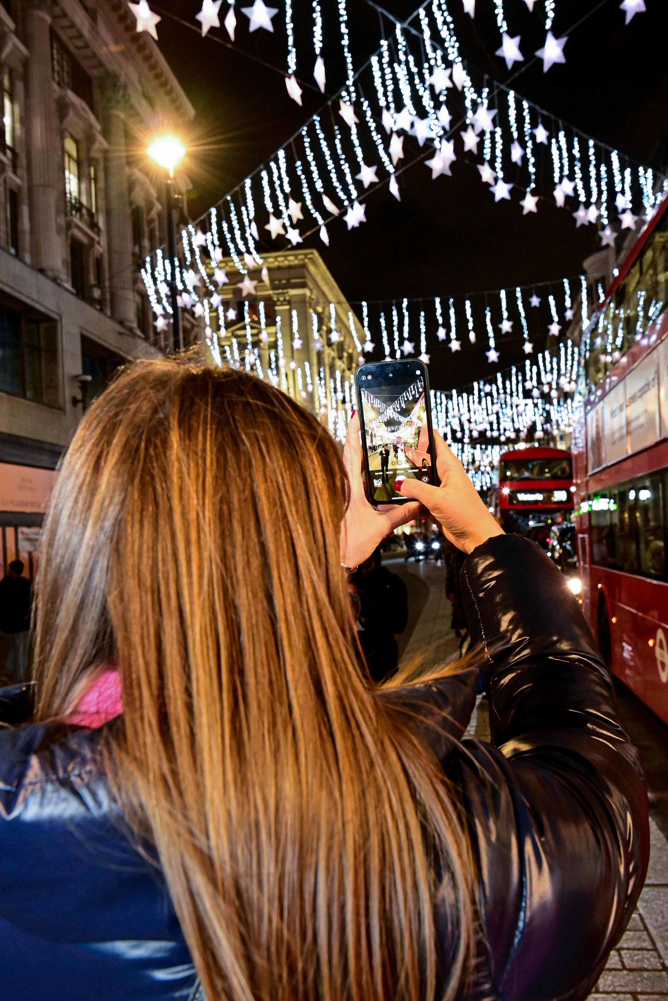 A woman takes a picture of the lights on Oxford Street