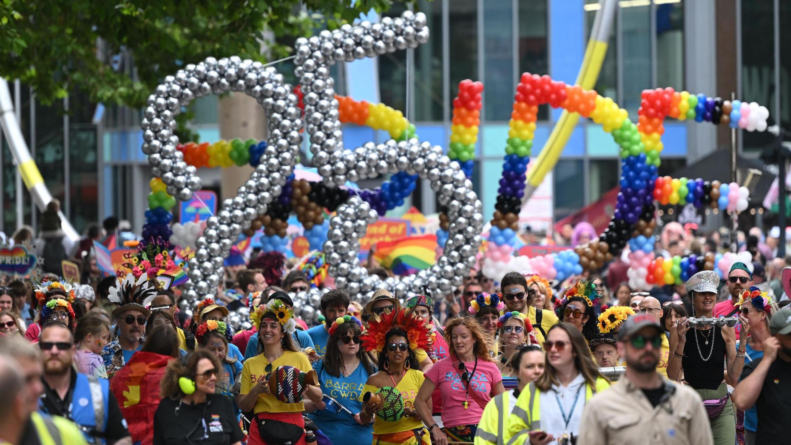 A crowd of people walking through the city centre with a silver balloon sculpture which says 25