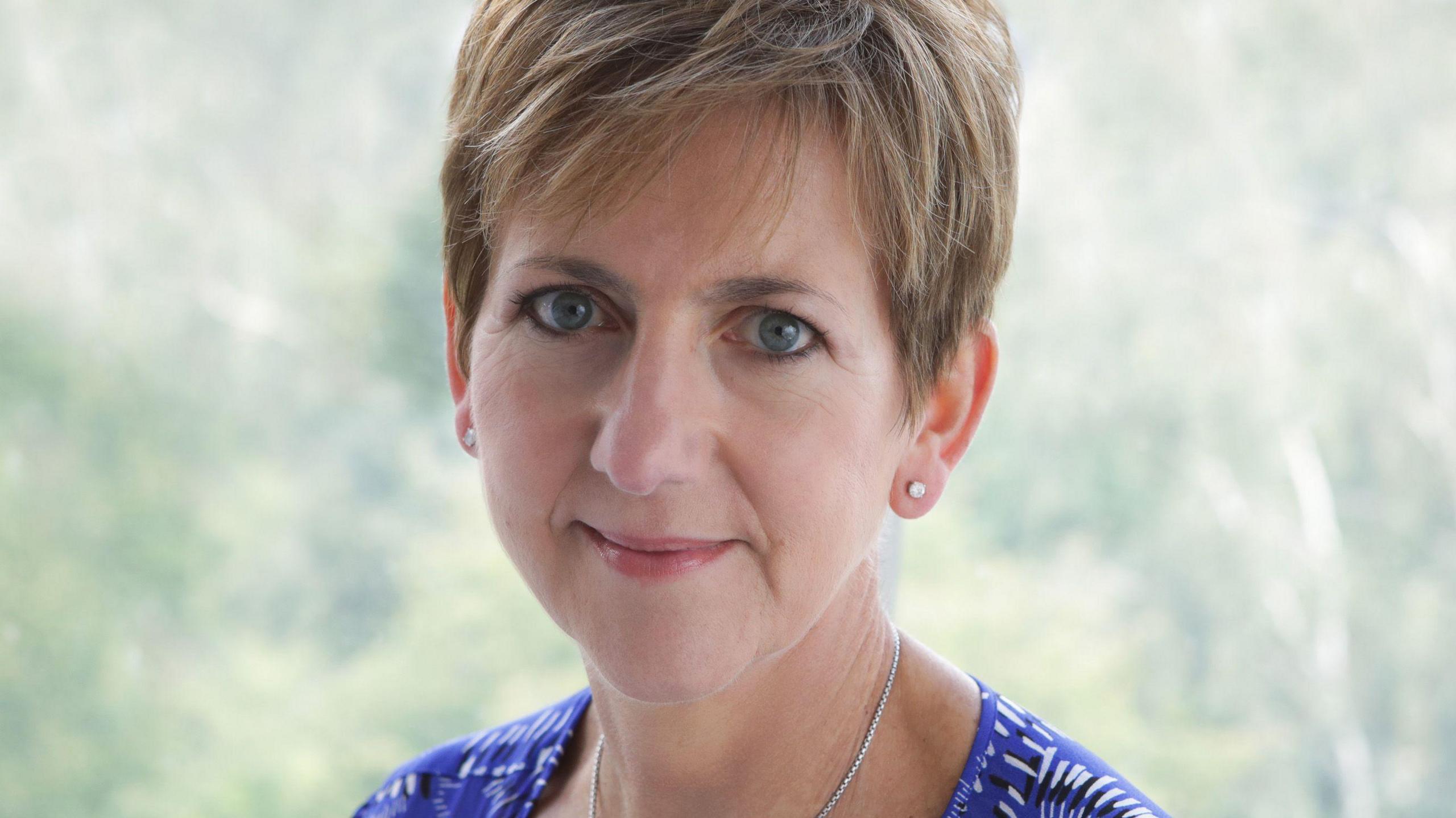 Dr Carole Gilling-Smith has short light brown hair. This is a head and shoulders photo. She wears a blue and white patterned top and a silver necklace. 