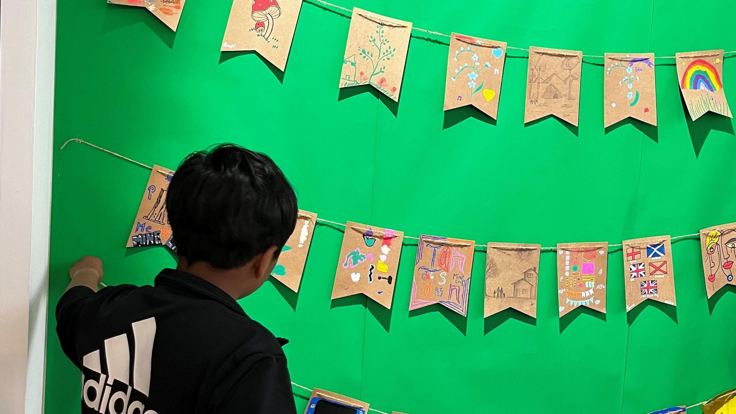 The back view of a boy haning up a string of handmade bunting against a green backdrop 