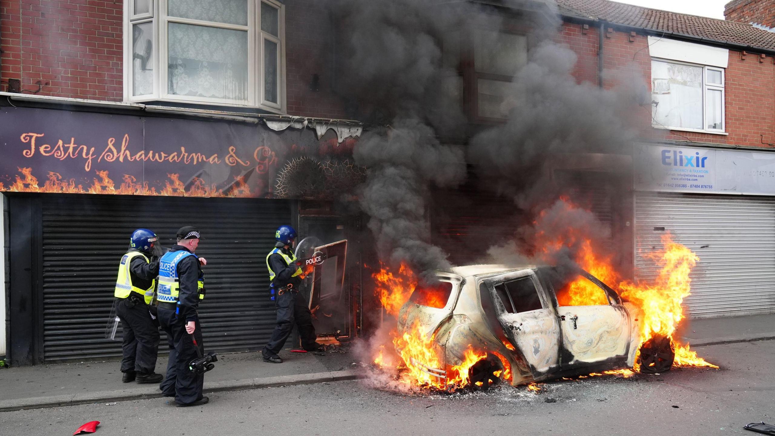 Police next to a burning car on Parliament Road