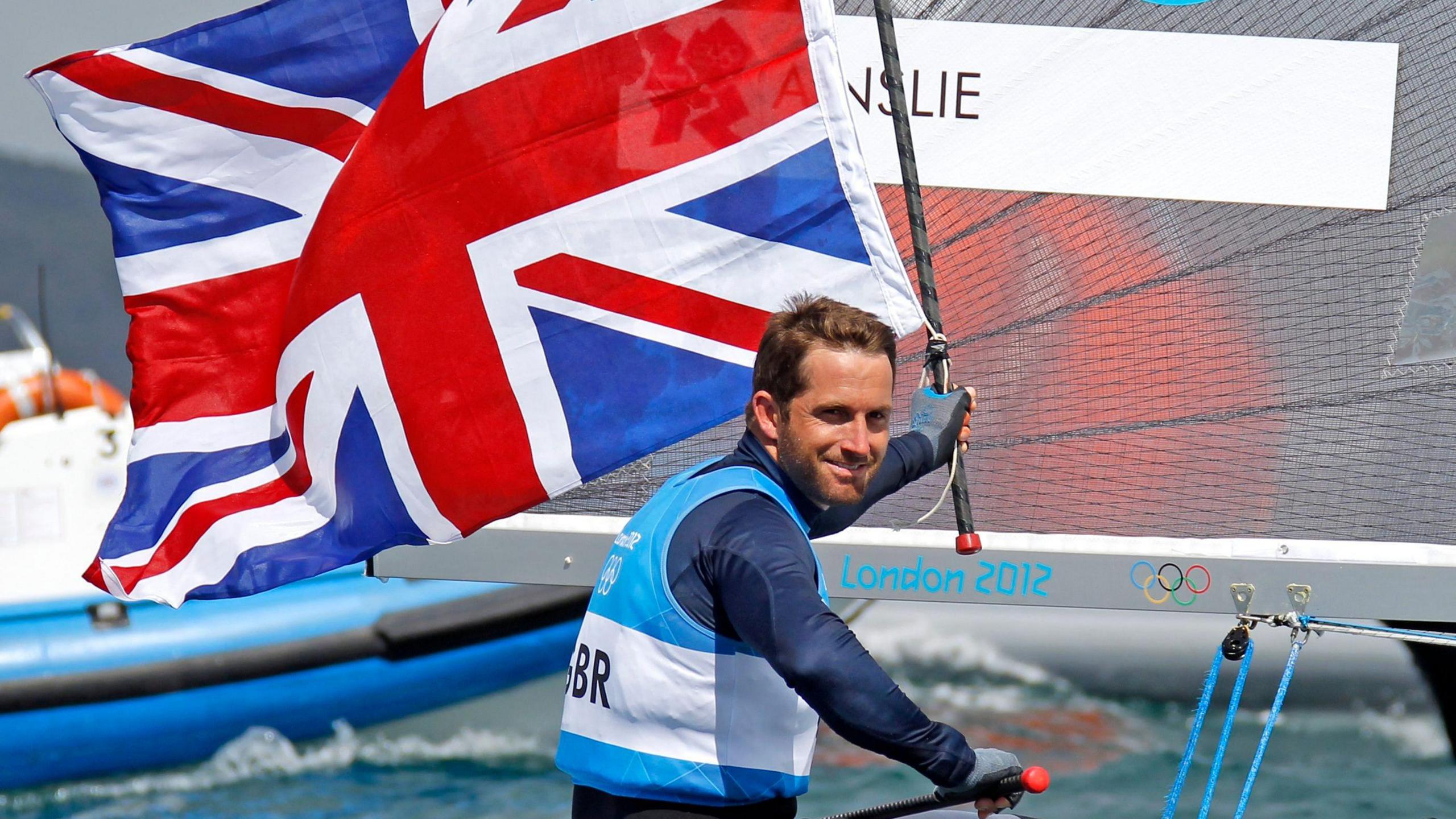 Sir Ben Ainslie holding Union Jack flag on board at boat at the 2012 Olympics in Weymouth