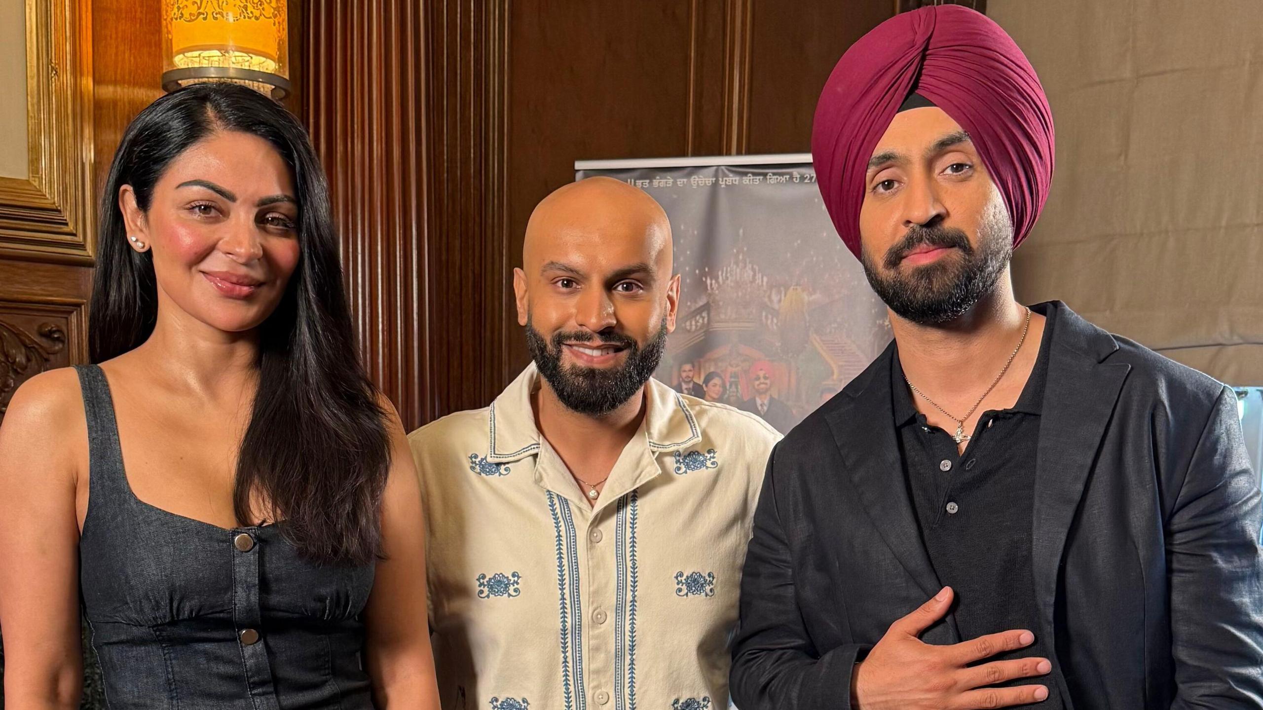 Neeru Bajwa, Haroon Rashid and Diljit Dosanjh together posing in front of a banner for their new film called Sardaar Ji 3.