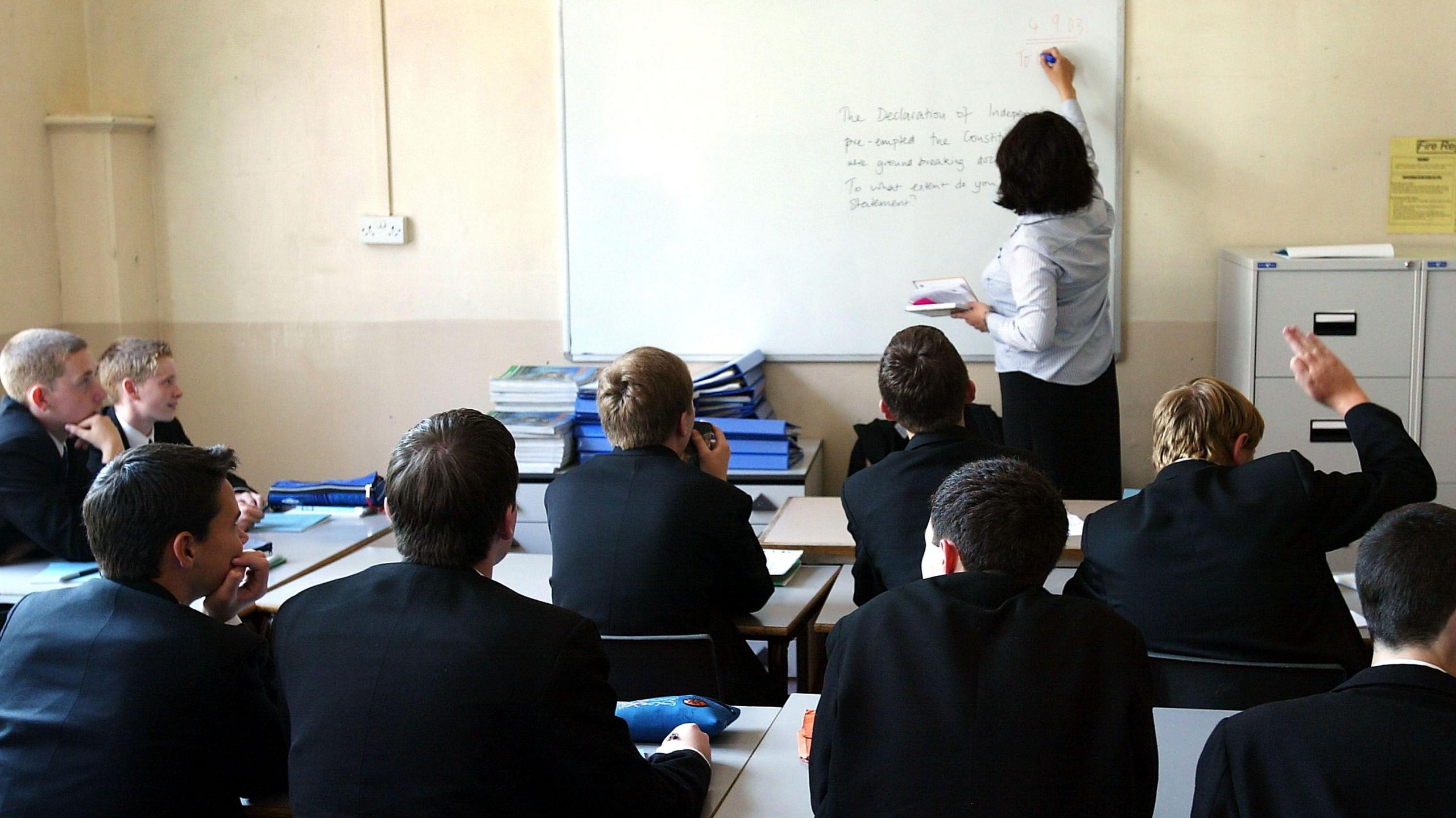 A classroom of boys facing a teaching writing on a whiteboard.