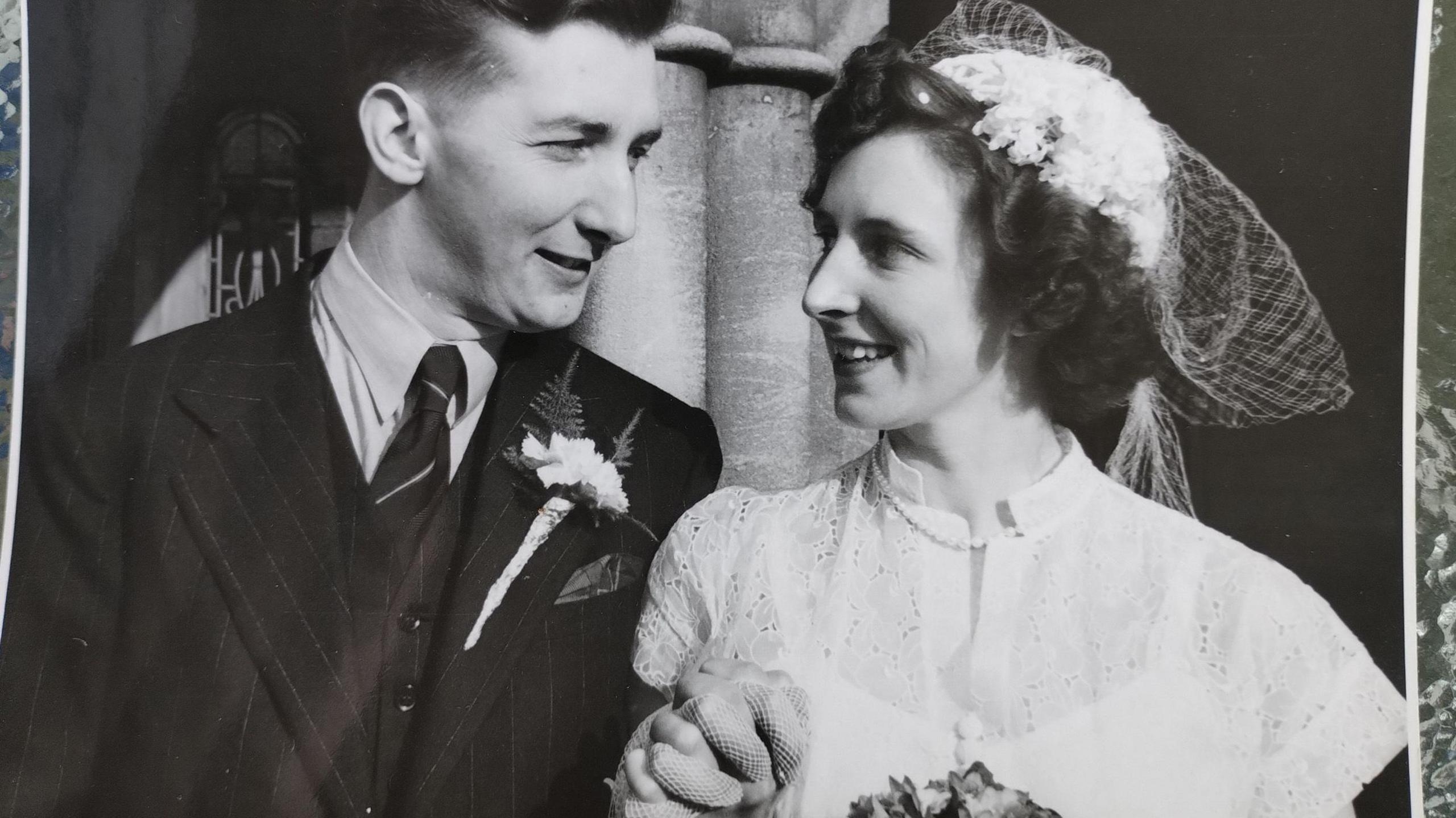 a black and white photo of a couple clasping hands and gazing lovingly at each other after getting married