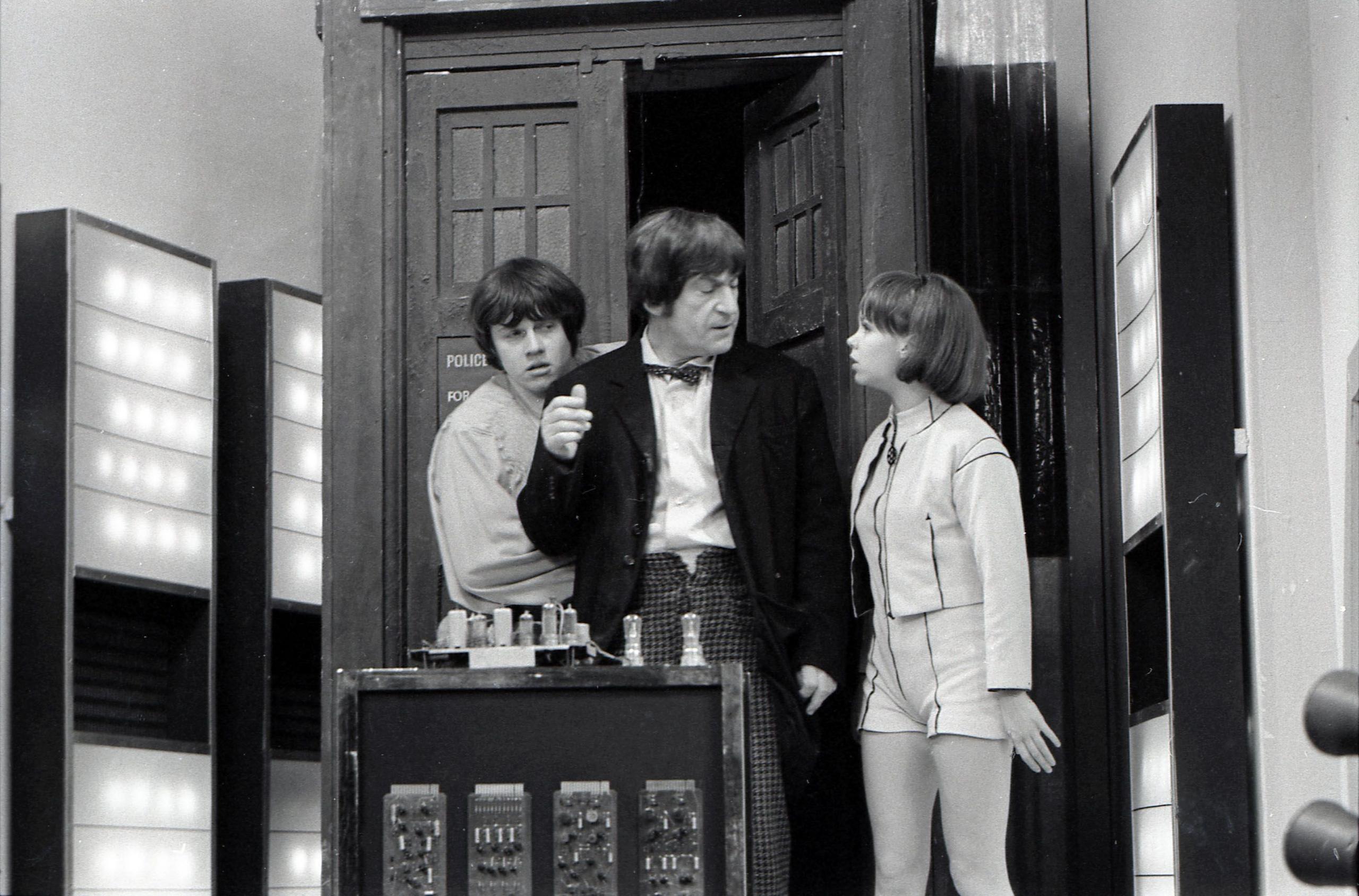 Black and White photo of Frazer Hines, Patrick Troughton and Wendy Padbury standing in front of the TARDIS with some futuristic looking equipment