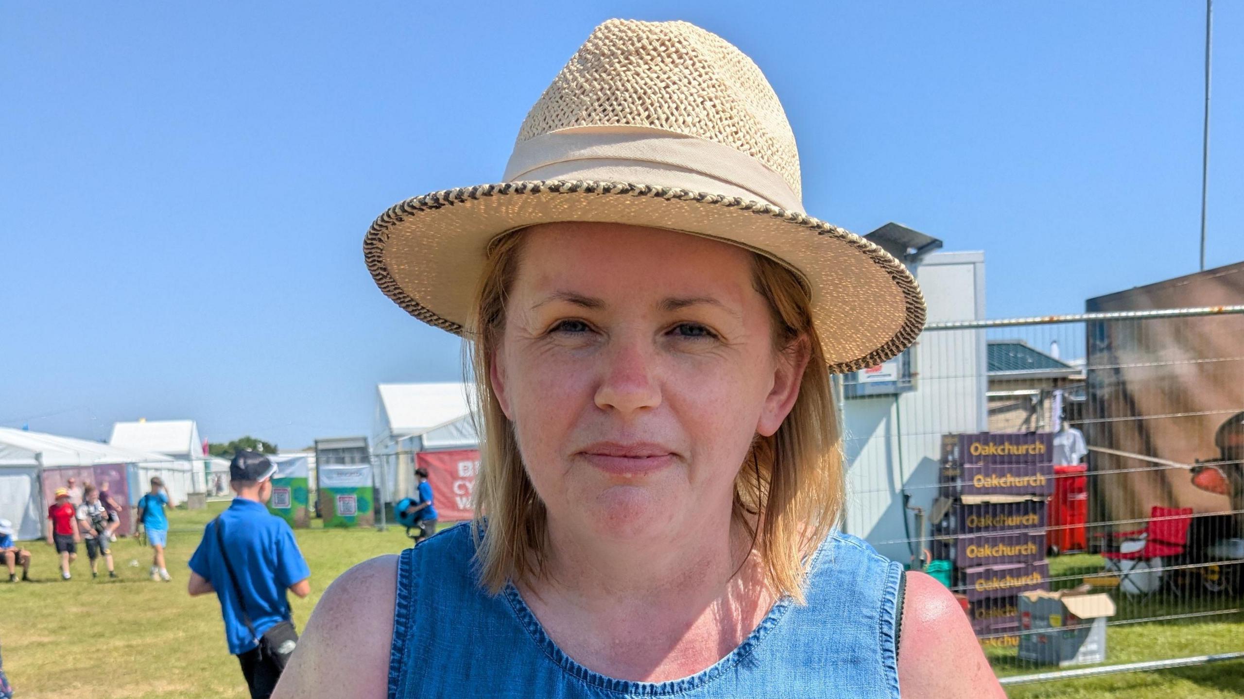 Sonia ar y maes yn gwisgo het gyda stondinau yn y cefndir. 