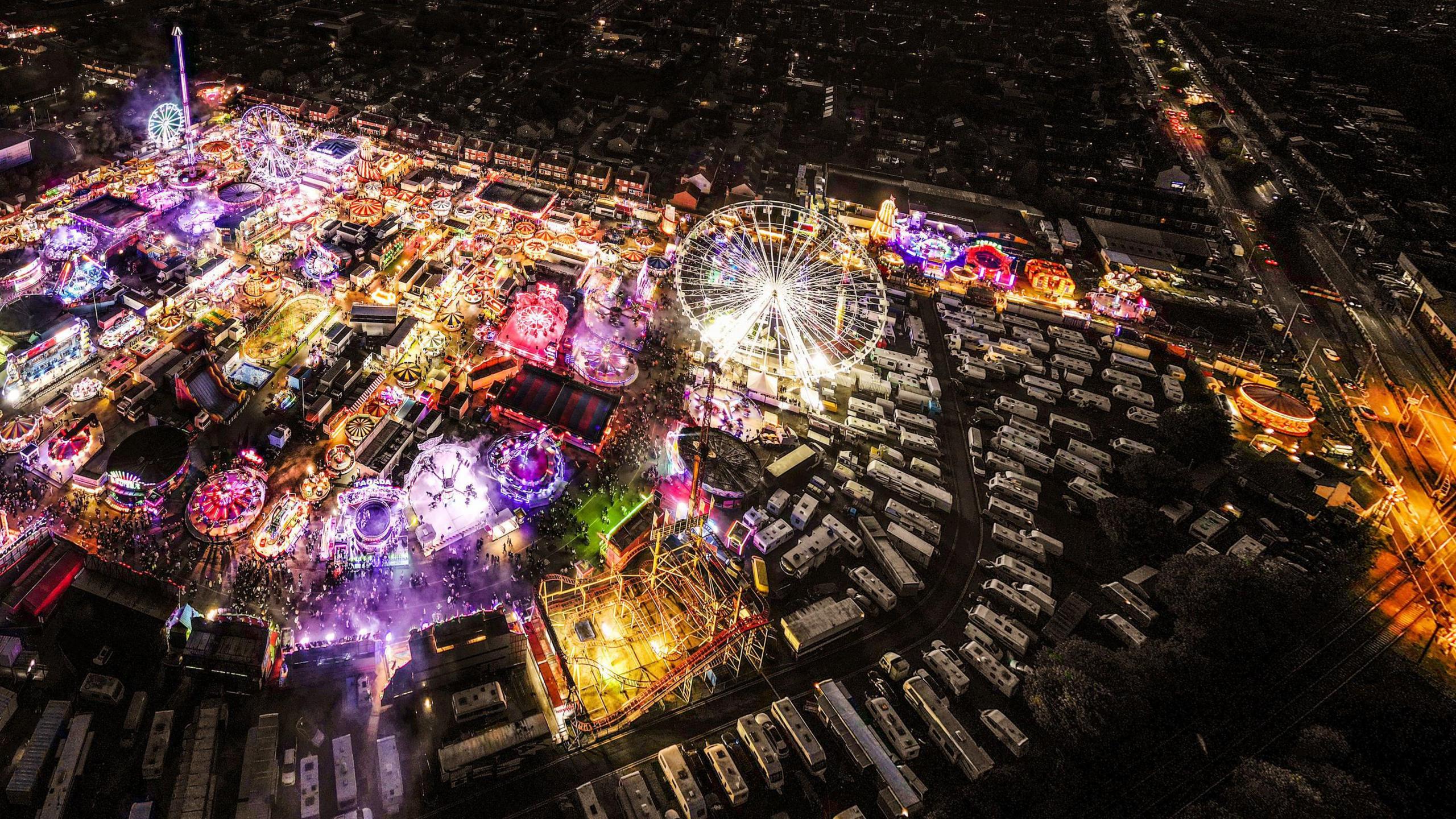 Aerial shot of Hull Fair, which is lit up in many colours at dusk, and surrounding residential streets.