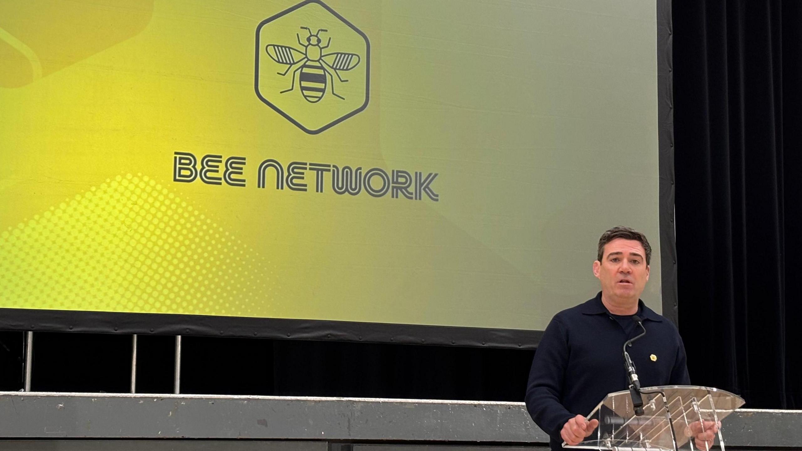 Andy Burnham at a podium dressed in black