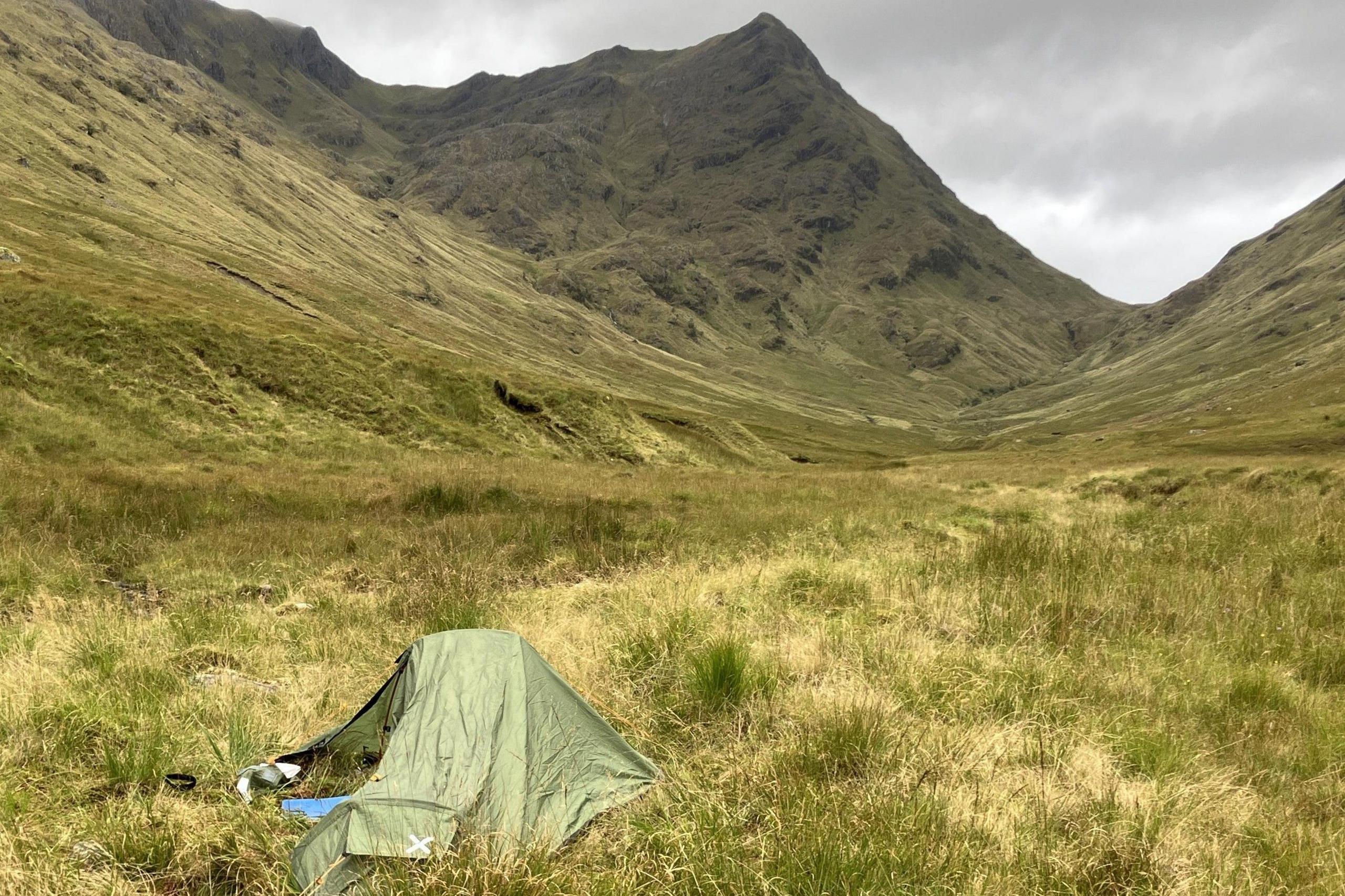 There is a small green tent surrounded by grass with mountains all around it.