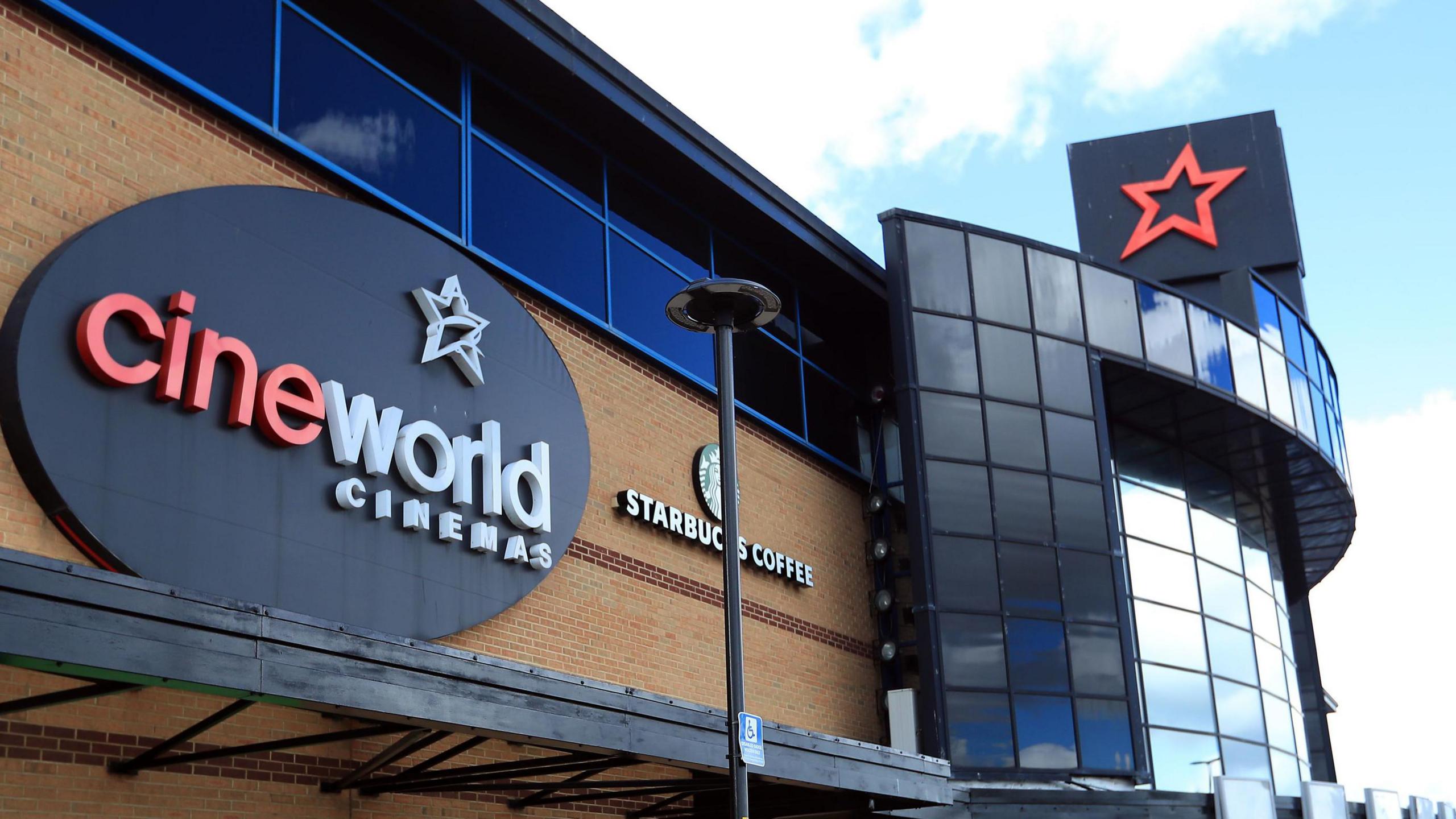 The outside of a Cineworld Cinema complex. A logo of the company is on the outside of the building which is a black oval with a white star and red and white writing which says cineworld CINEMAS.